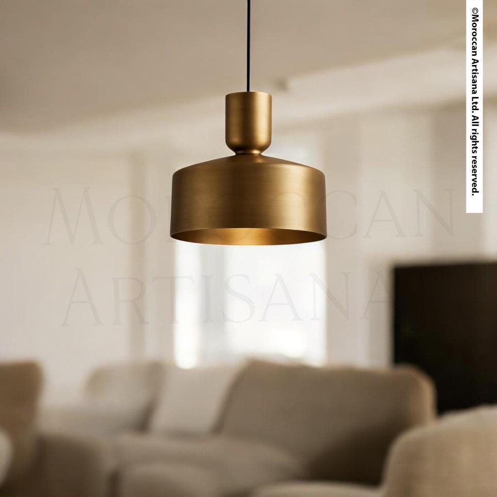 A modern gold pendant lamp hangs from the ceiling in a minimalist living room, casting a warm glow over the space.
