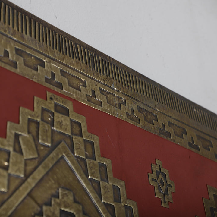 a close-up view of a decorative metal surface with a red background and intricate geometric patterns.