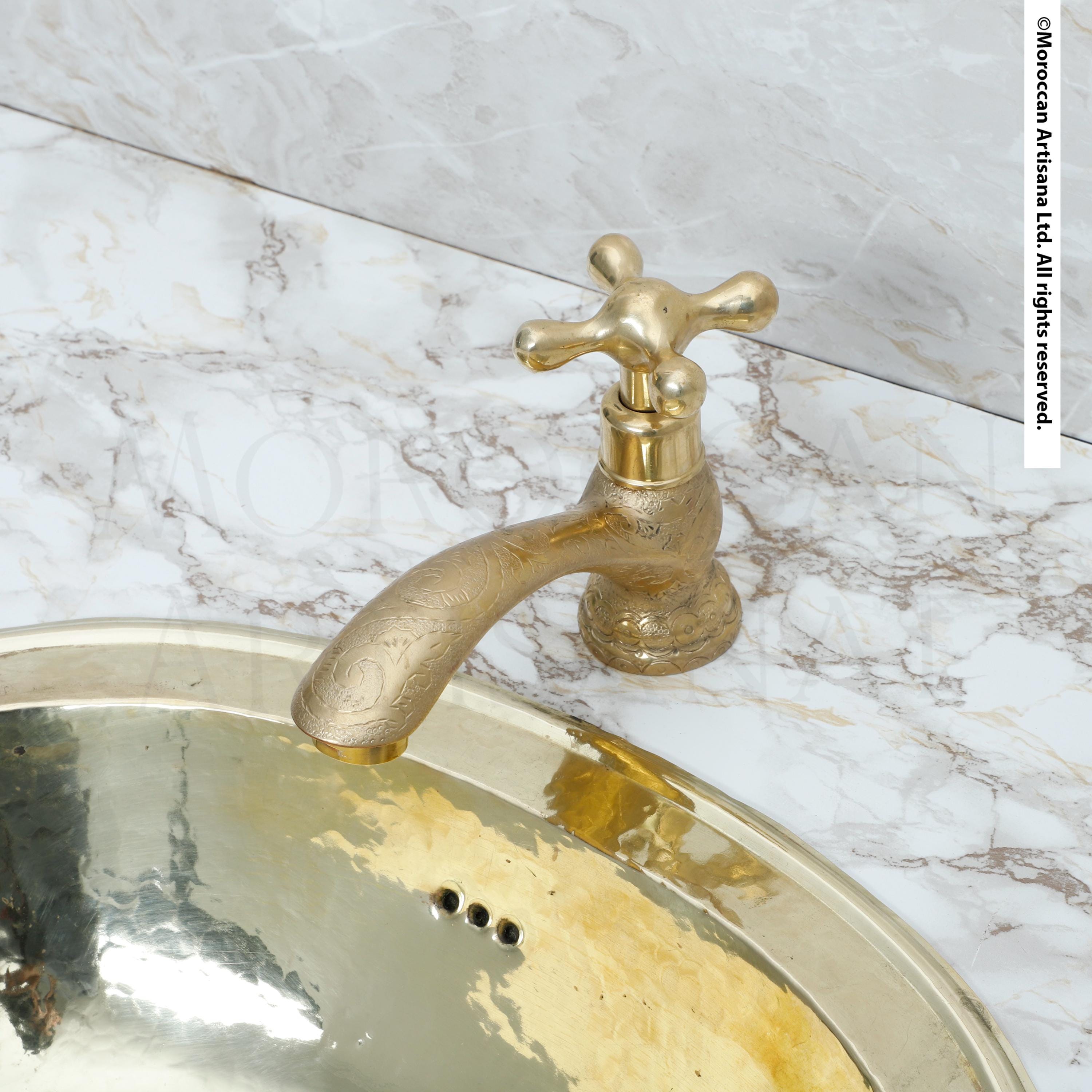 a gold-colored faucet with a decorative handle, situated above a marble countertop.