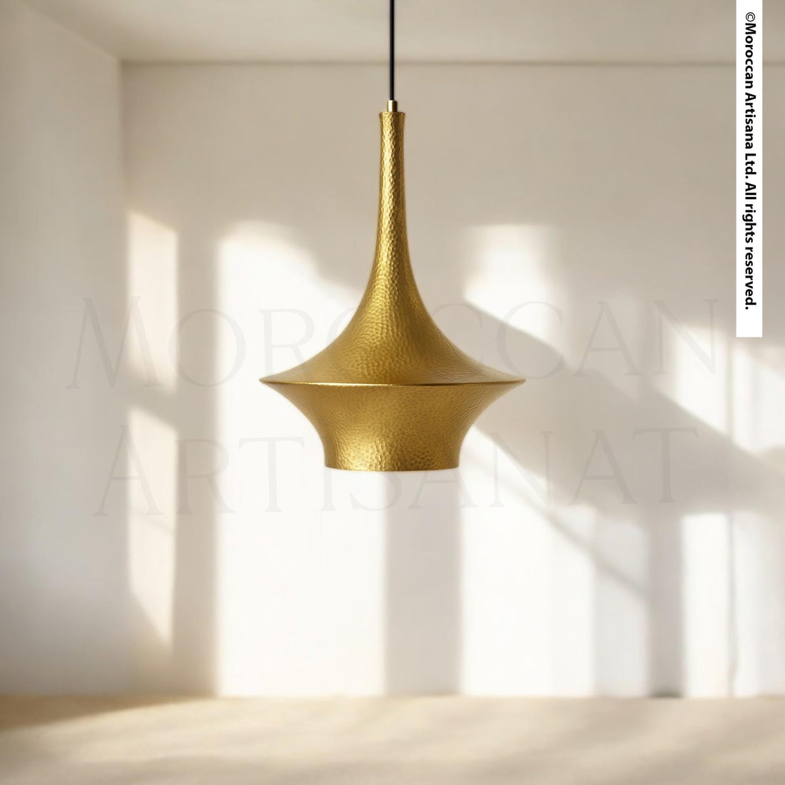 A gold-colored pendant light hangs from the ceiling in a minimalist room with white walls and a wooden floor.