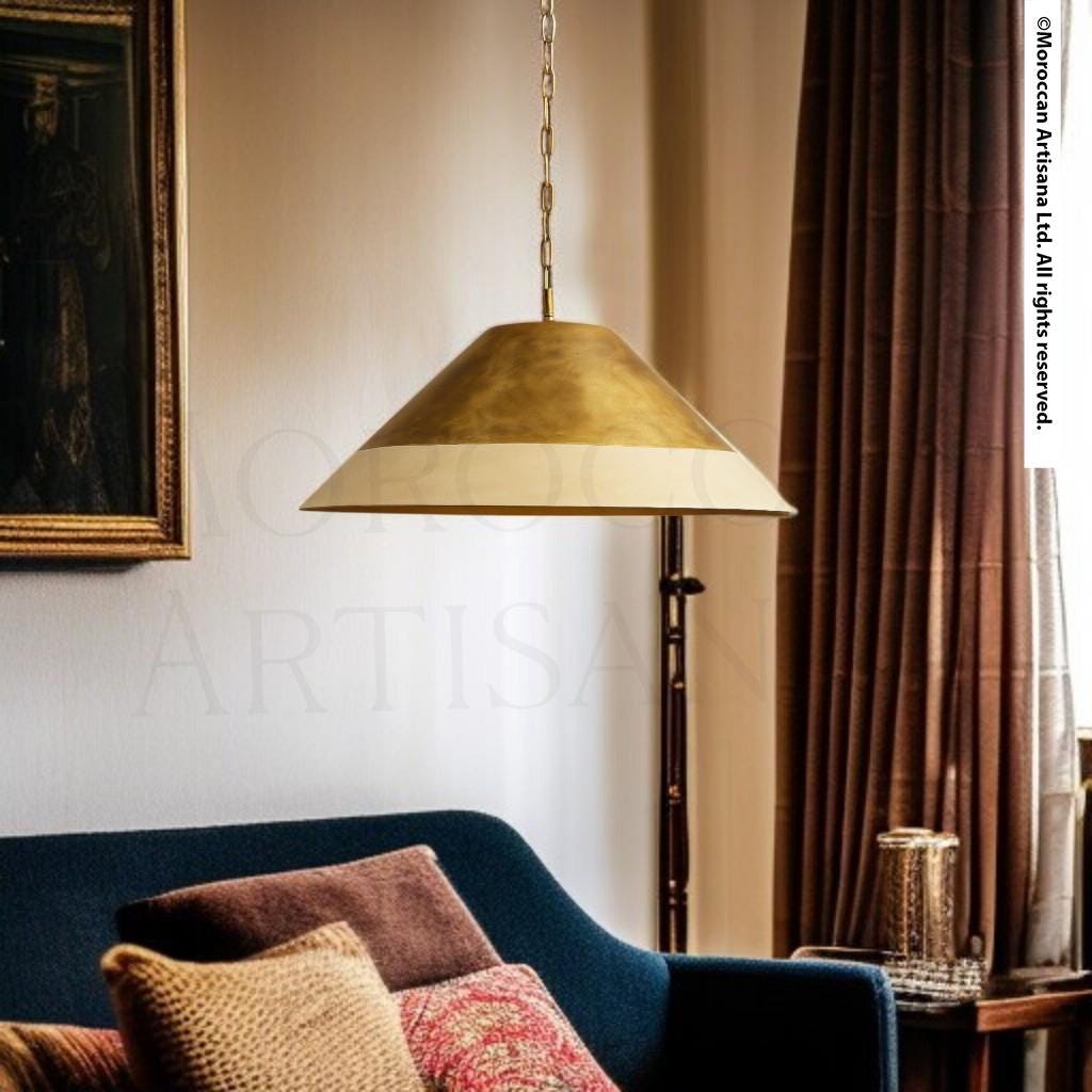 a modern living room with a gold-colored pendant lamp hanging from the ceiling, casting a warm glow over the space. The room is furnished with a blue sofa, a wooden side table, and a glass vase, creating a cozy and inviting atmosphere.