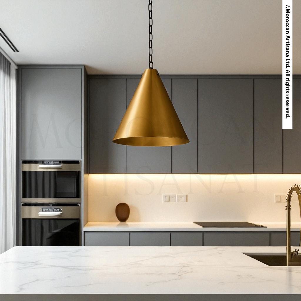 a modern kitchen with a sleek, minimalist design. The kitchen features gray cabinets, a white countertop, and a gold pendant light hanging above the counter. The overall color scheme is neutral, with the gold accent adding a touch of luxury and sophistication.