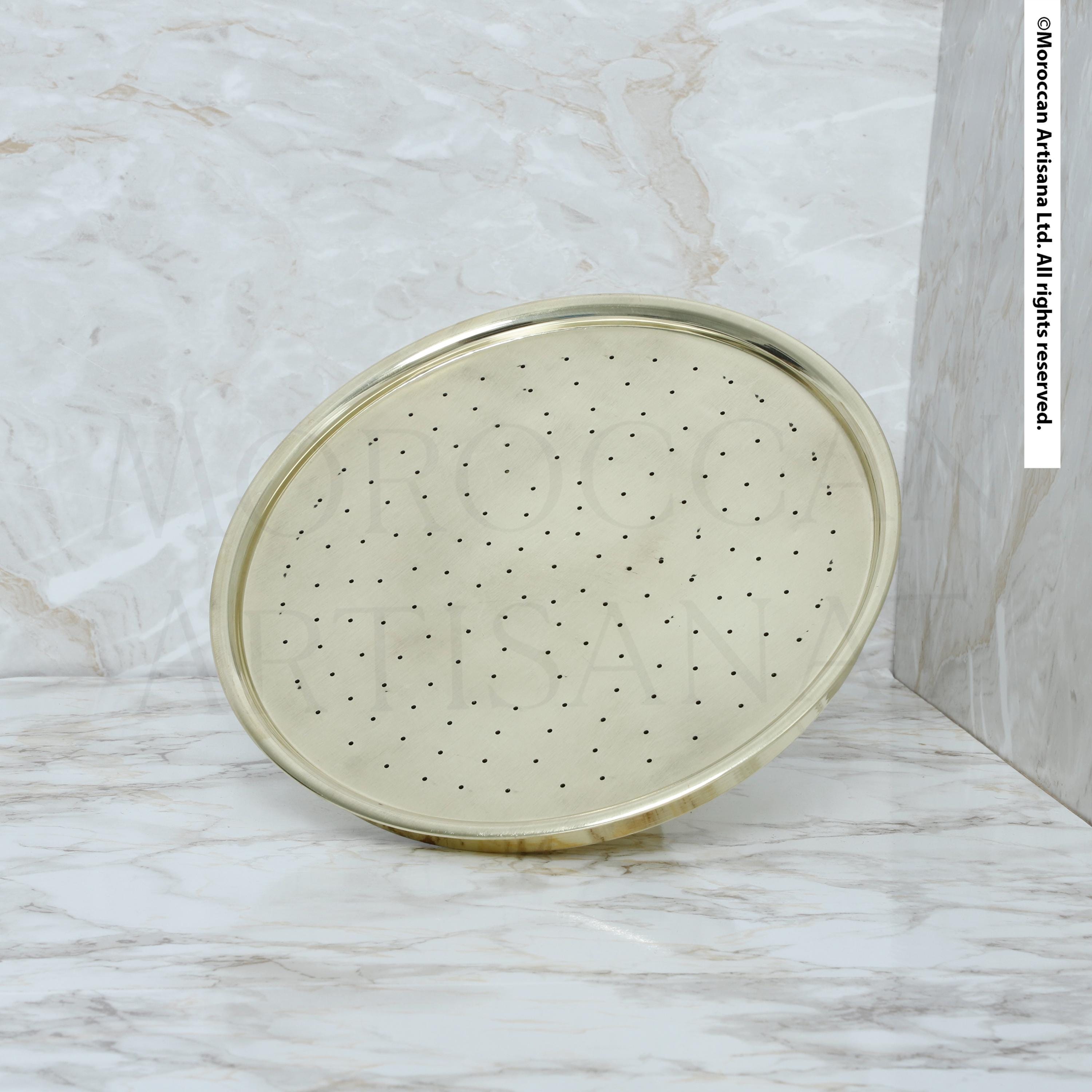 A round, gold-colored shower head with small holes is shown against a marble background.