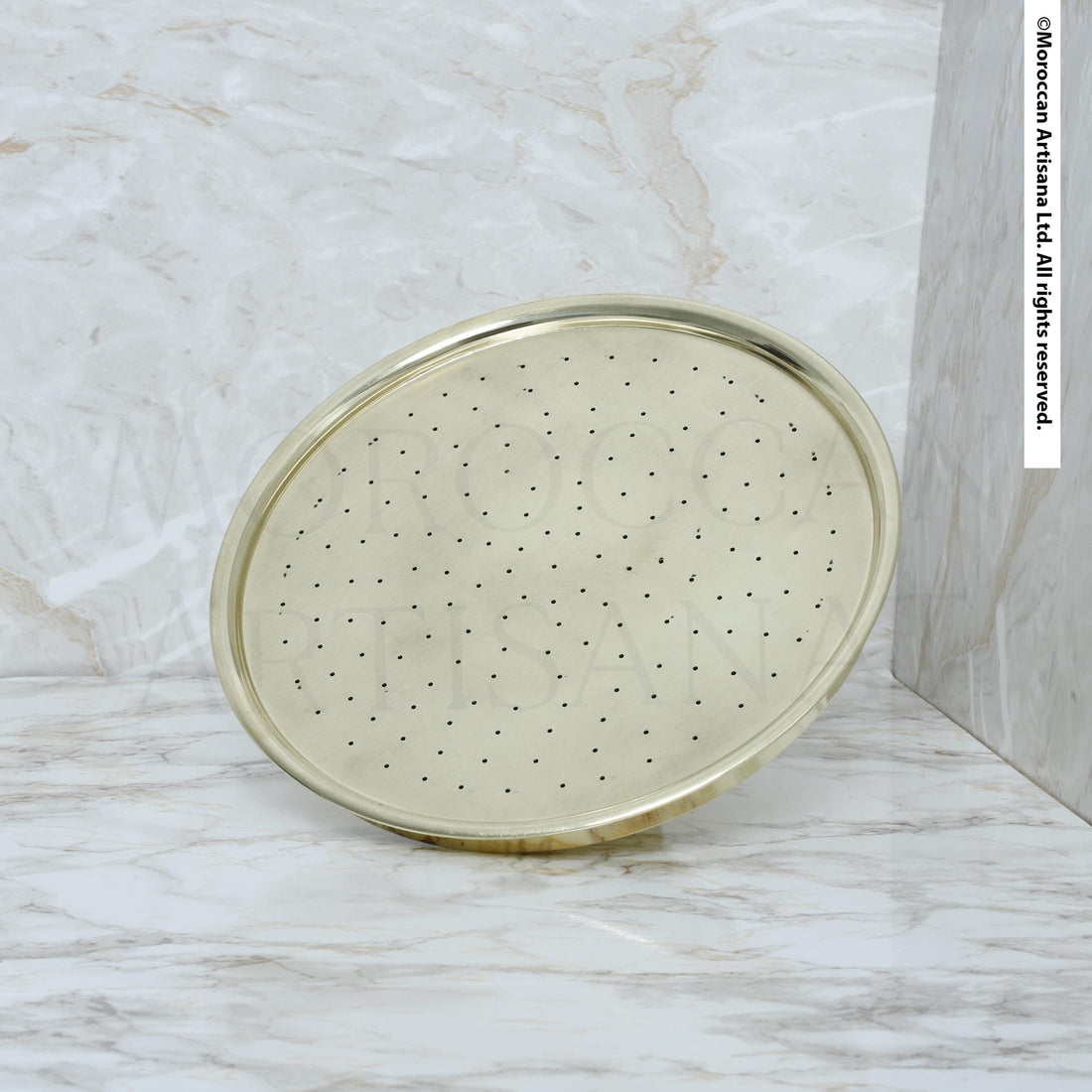A round, gold-colored shower head with small holes is shown against a marble background.