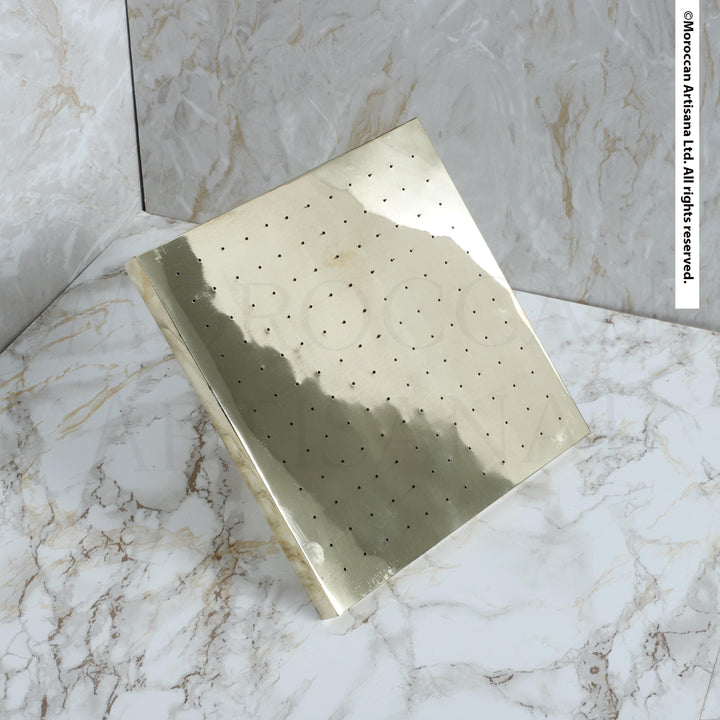 a square-shaped metallic object with a grid-like pattern on its surface, placed on a marble surface.