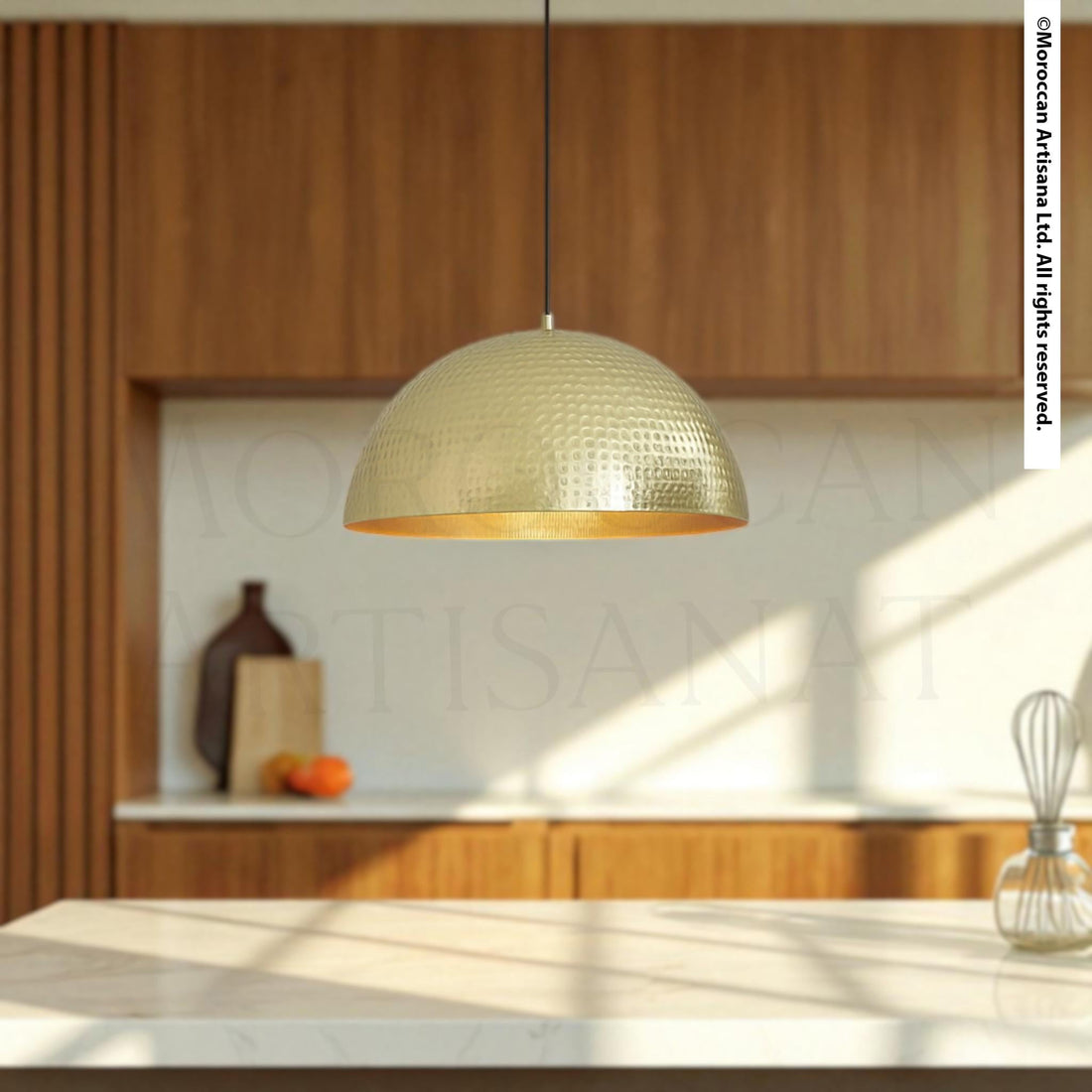 A modern kitchen with a large, round, gold-colored pendant light hanging from the ceiling, casting a warm glow over the wooden cabinets and countertop.