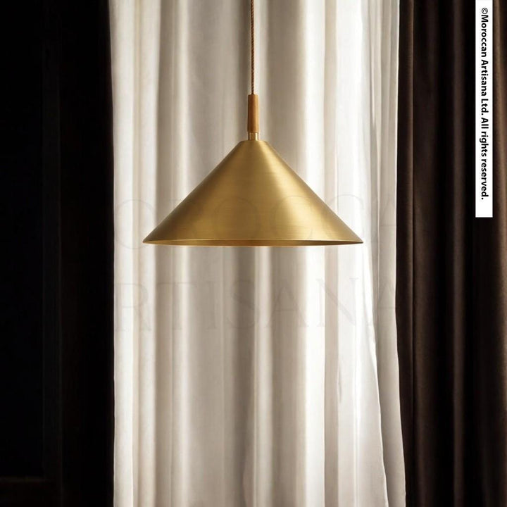 A gold pendant lamp hangs from a cord, suspended from a window with white curtains.