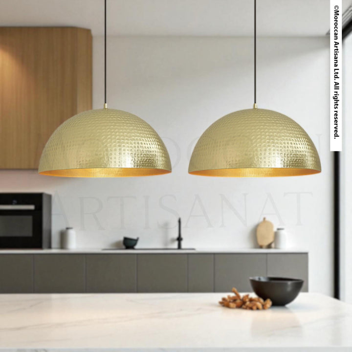 a modern kitchen with two gold-colored pendant lights hanging above a white countertop. The kitchen has a sleek, minimalist design with gray cabinets and a black bowl on the countertop.