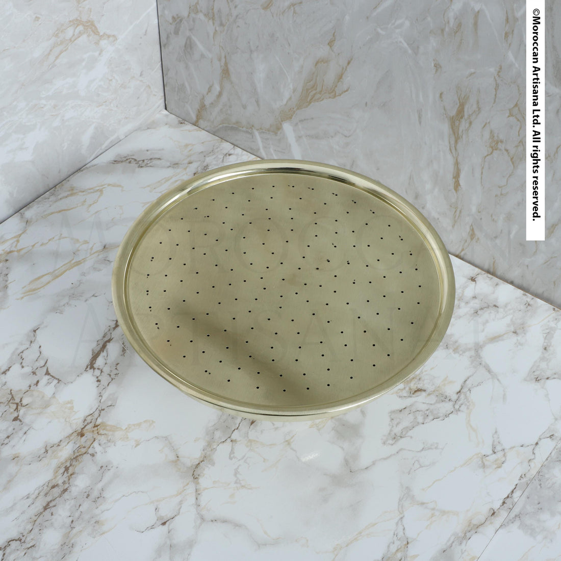 a round, metallic shower head with a perforated design, placed on a marble countertop.