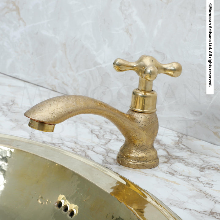 A gold-colored bathroom faucet with a decorative handle is shown against a marble countertop.