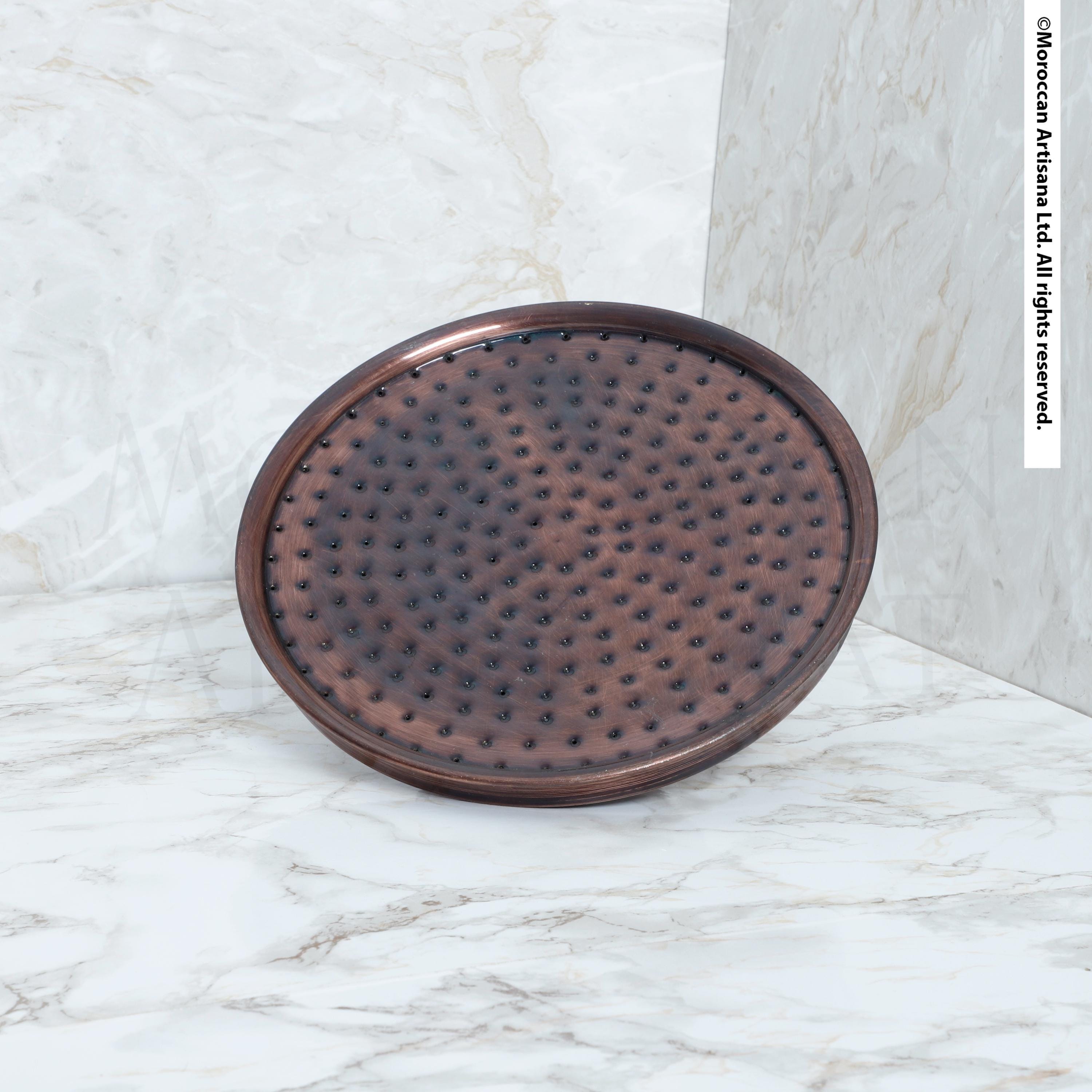 a round, metallic shower head with a textured surface, placed on a marble countertop.