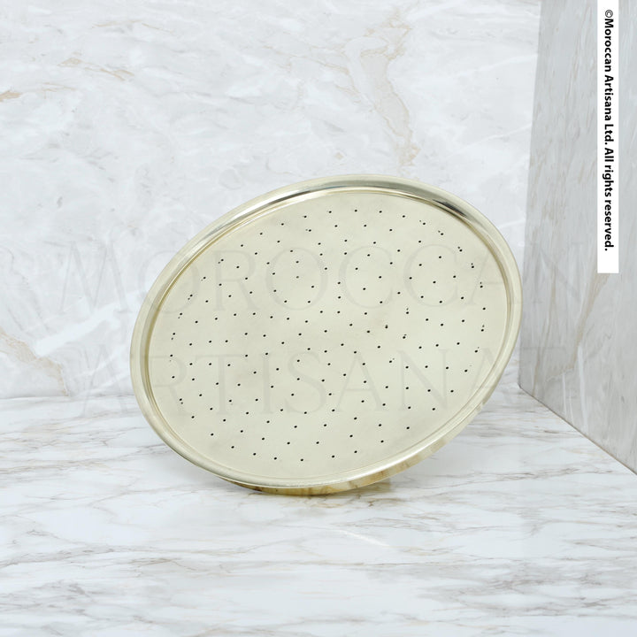 A round, gold-colored shower head with small holes is shown against a marble background.