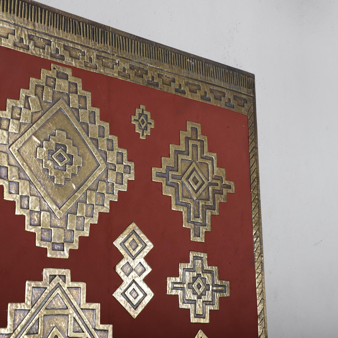a close-up view of a red surface adorned with intricate geometric patterns in gold and silver. The patterns include various diamond shapes and other geometric designs, creating a visually striking and detailed appearance.