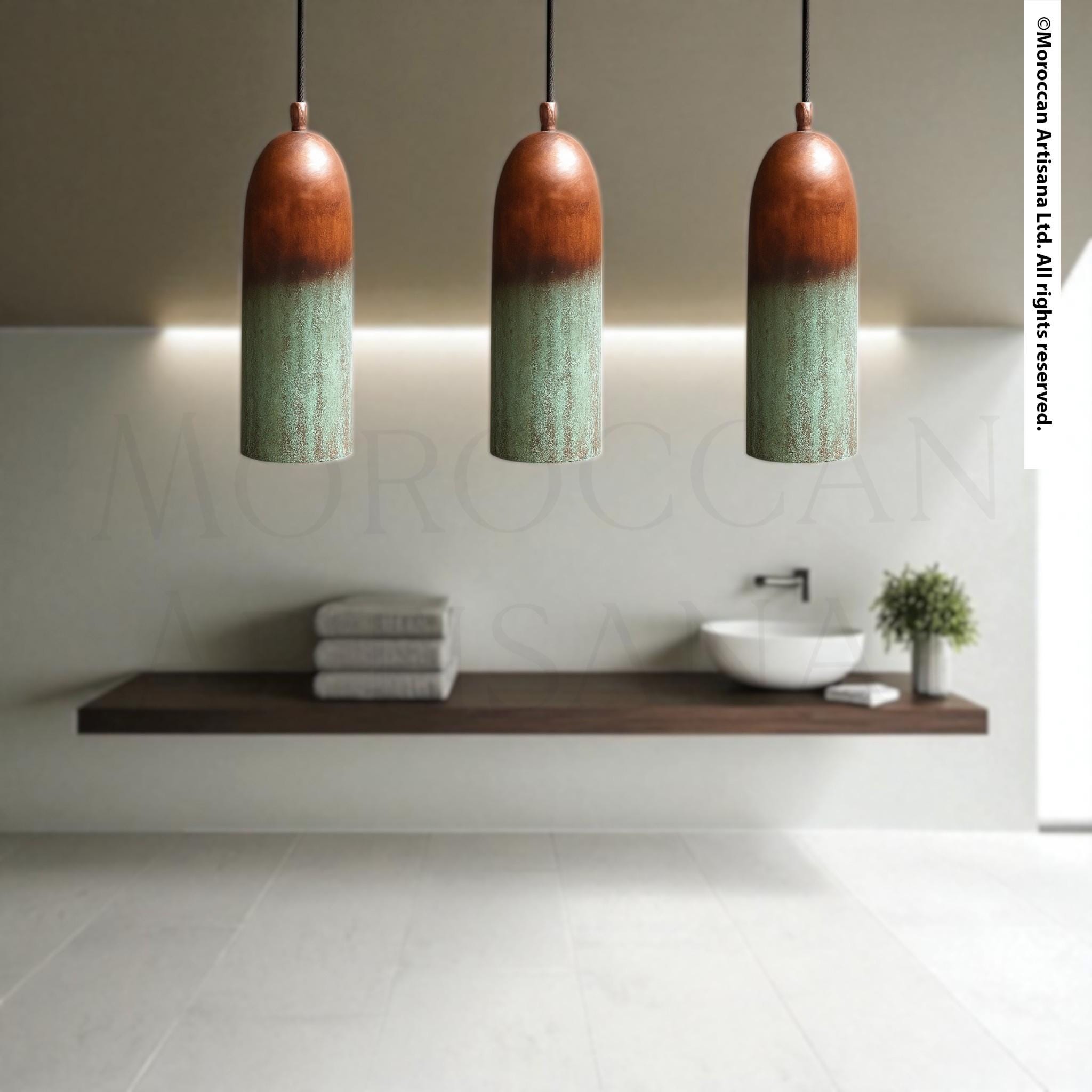 a modern bathroom with a wooden shelf and three hanging pendant lights. The pendant lights have a green and brown color scheme and are suspended from the ceiling. The bathroom has a minimalist design, with a white sink and a plant on the shelf.