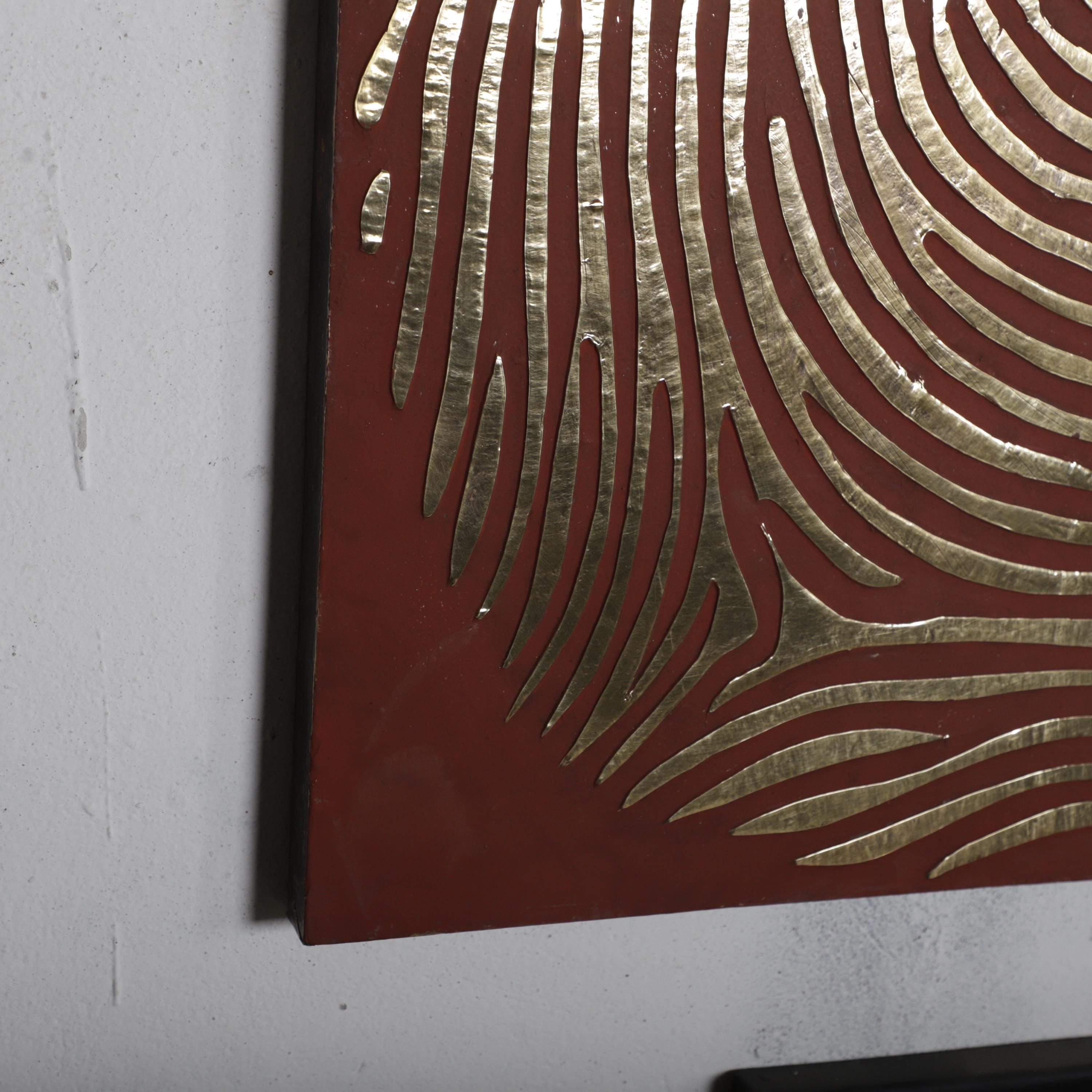 a close-up view of a red surface with a gold-colored, abstract pattern resembling a fingerprint design.