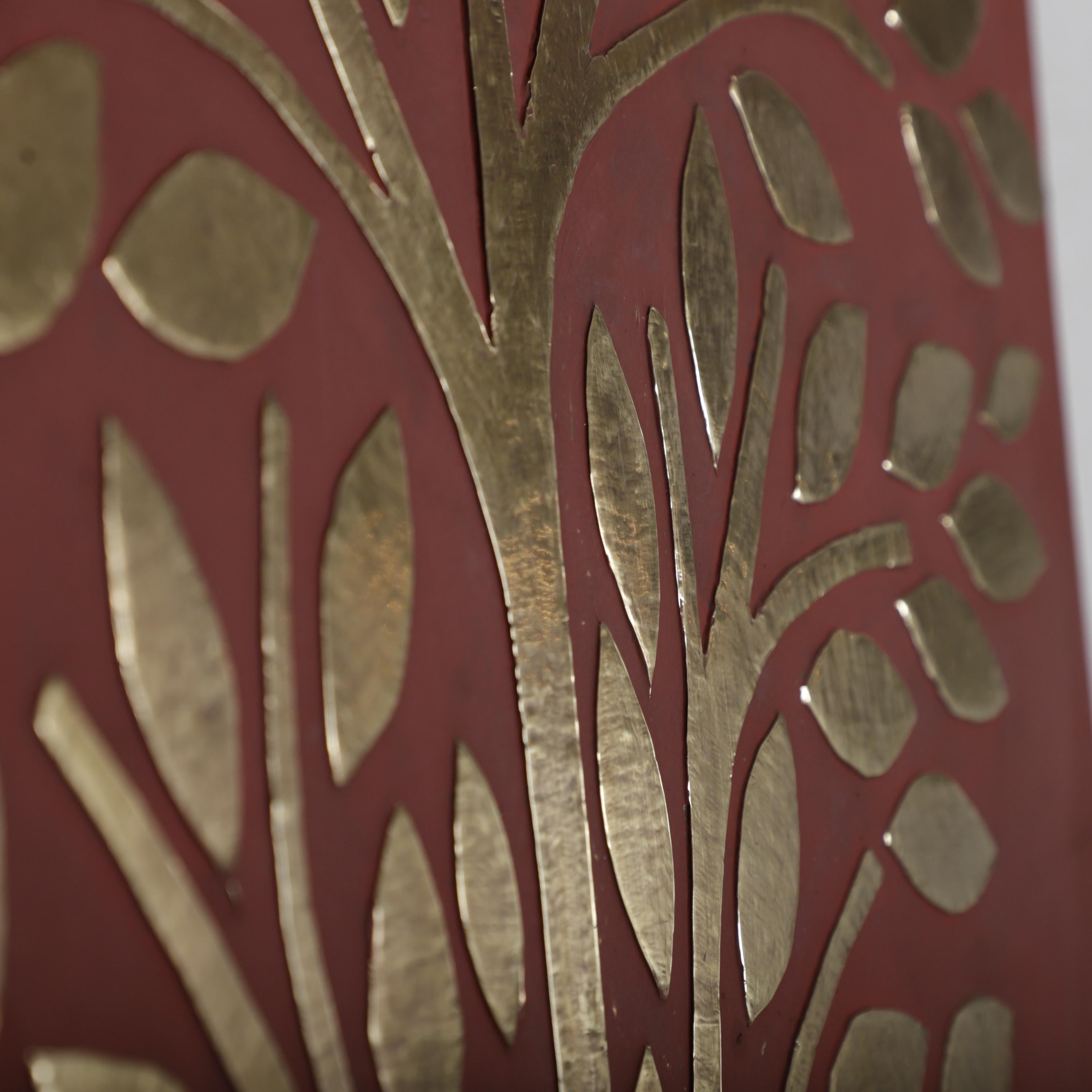 a close-up view of a red surface with a gold tree design. The design consists of various shapes resembling leaves and branches, creating a visually striking contrast against the red background.
