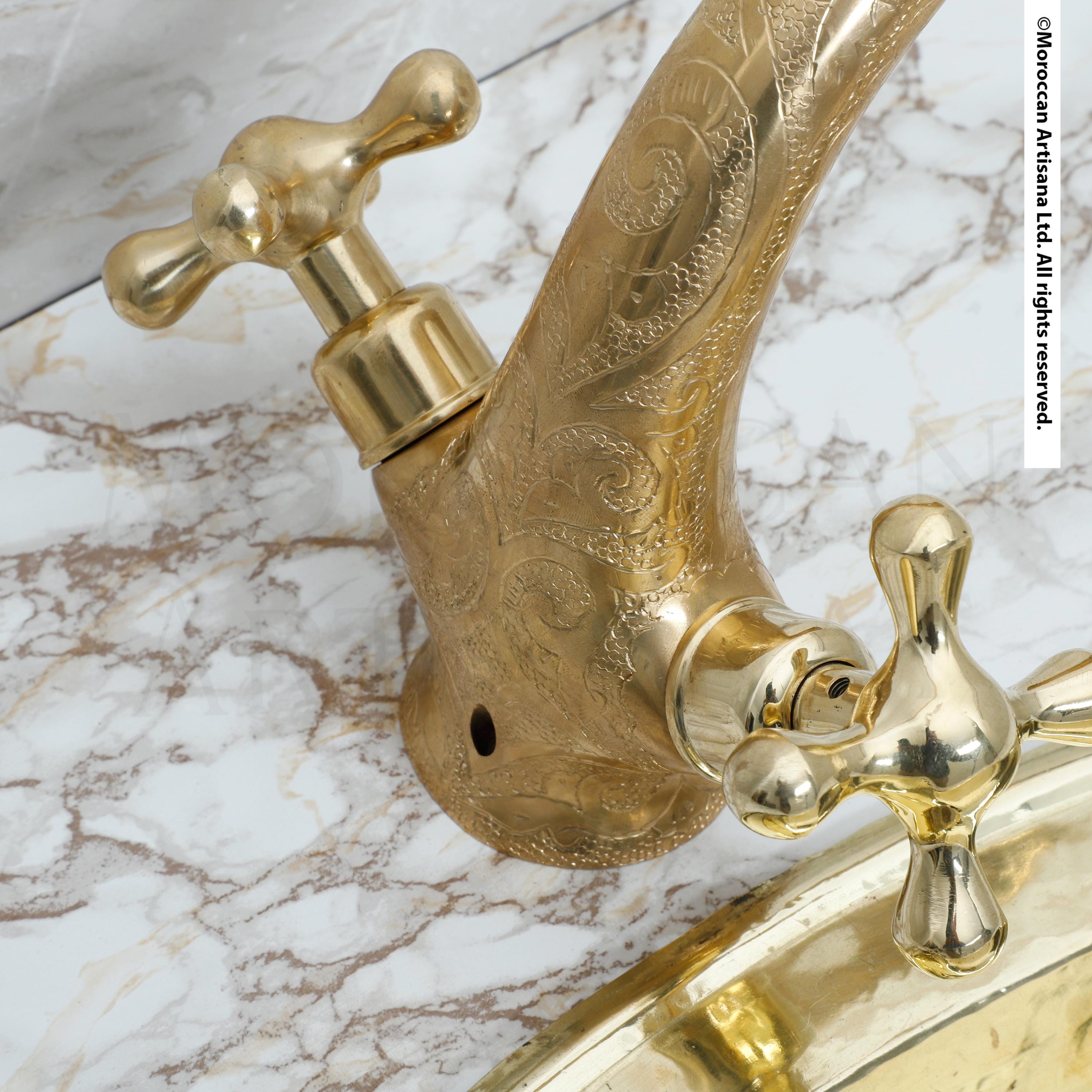 A close-up view of a decorative gold faucet with ornate patterns on its surface, set against a marble background.