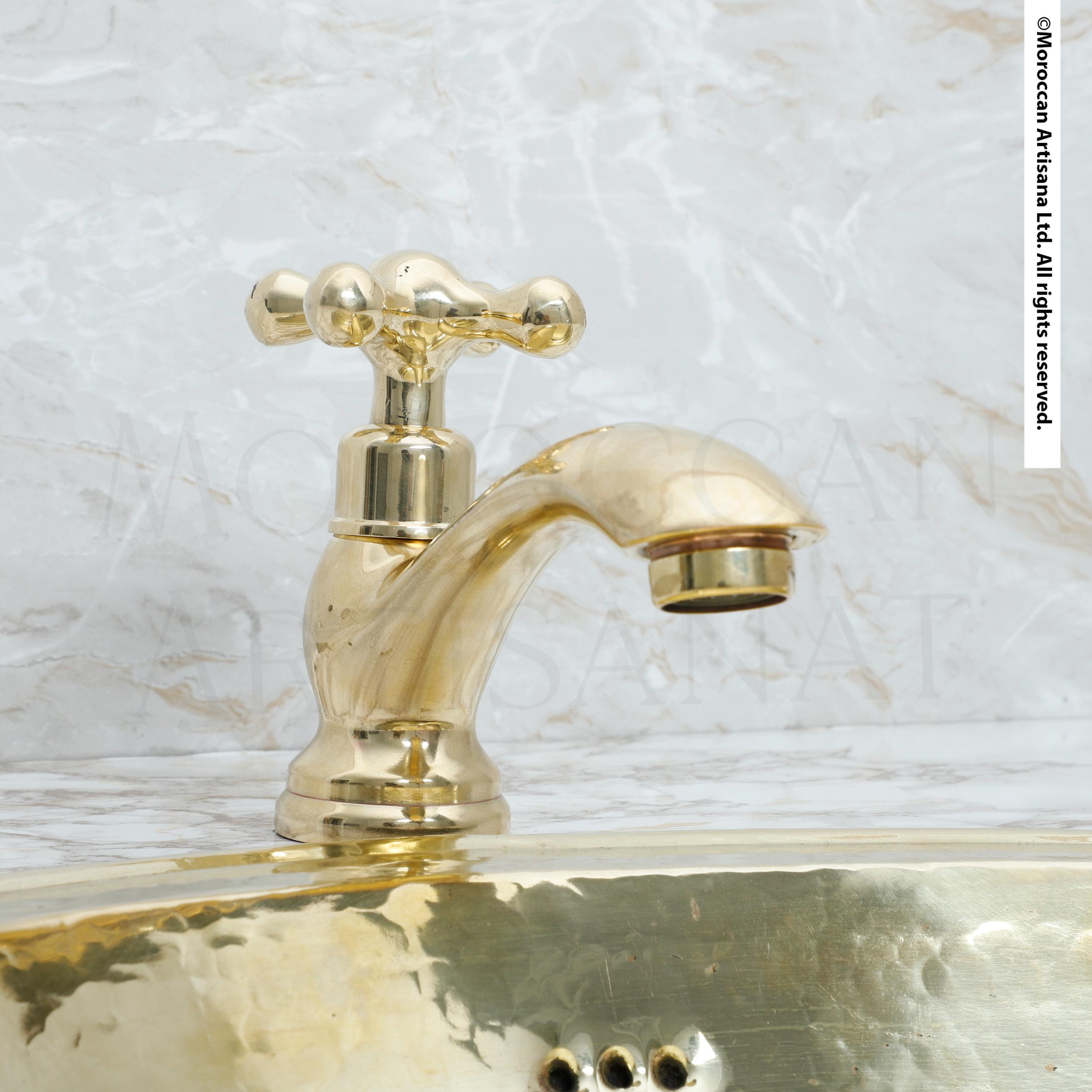 A shiny gold-colored faucet is mounted on a marble countertop.