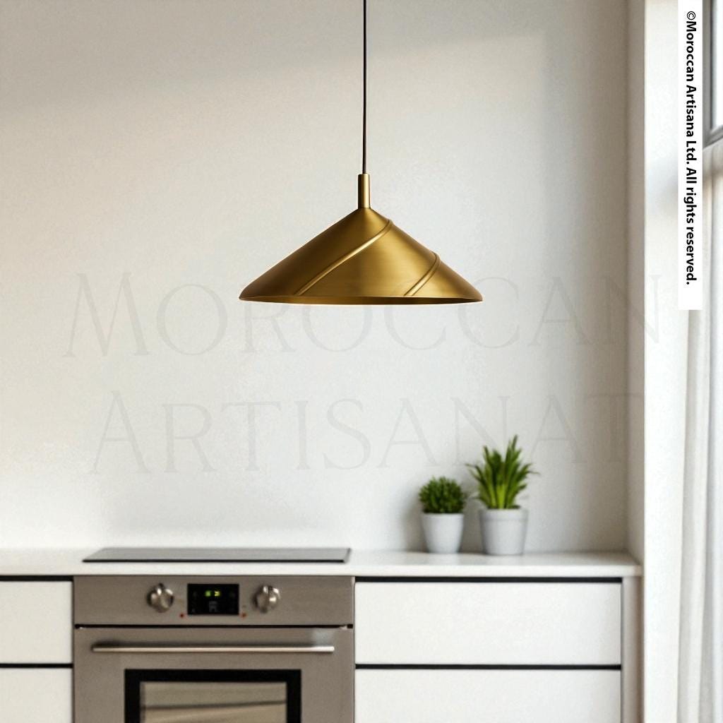 a modern kitchen with a sleek, gold pendant light hanging above a stainless steel oven. The kitchen has white cabinets and a white countertop, creating a clean and minimalist aesthetic.