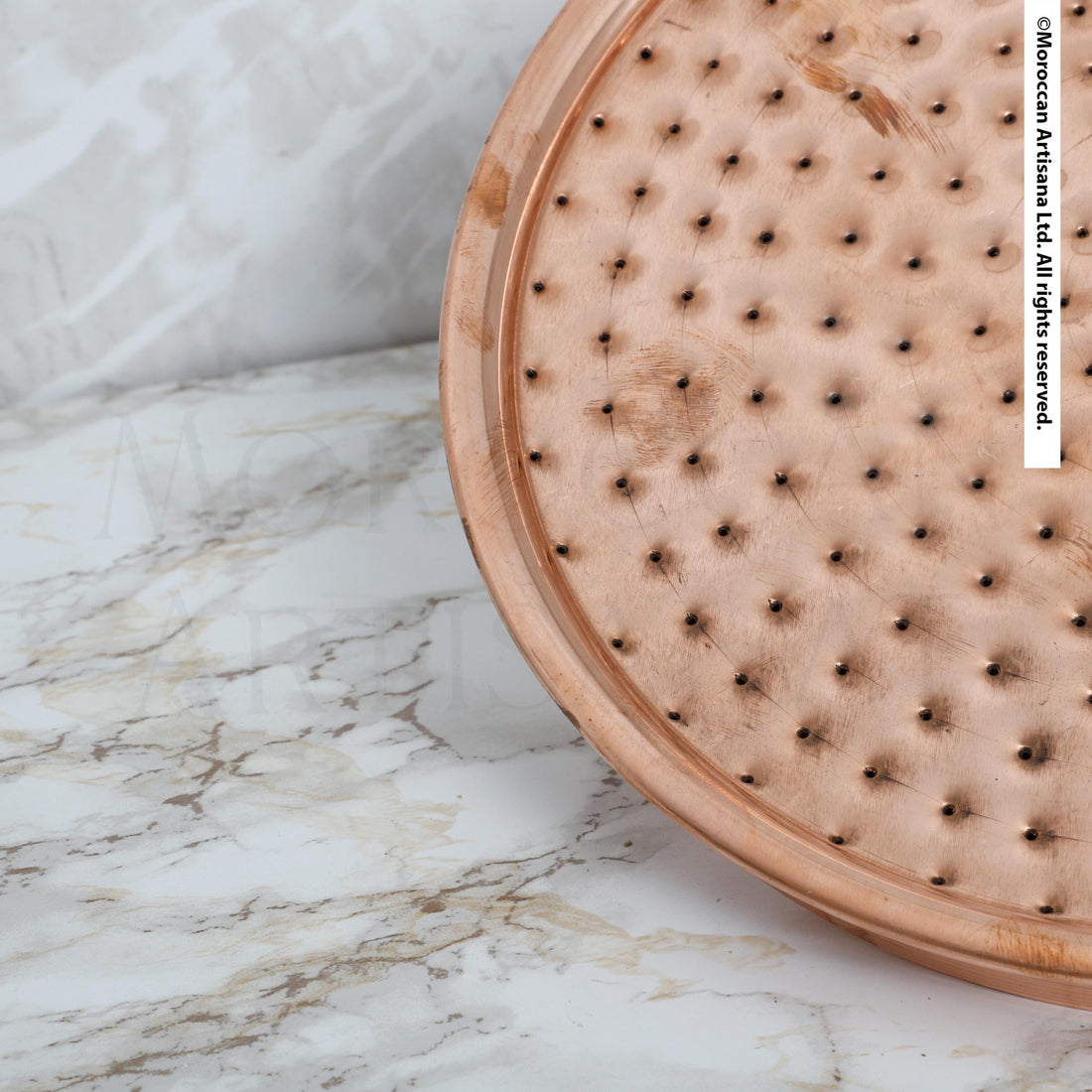 a close-up view of a copper-colored metal object with a textured surface, resting on a marble countertop.