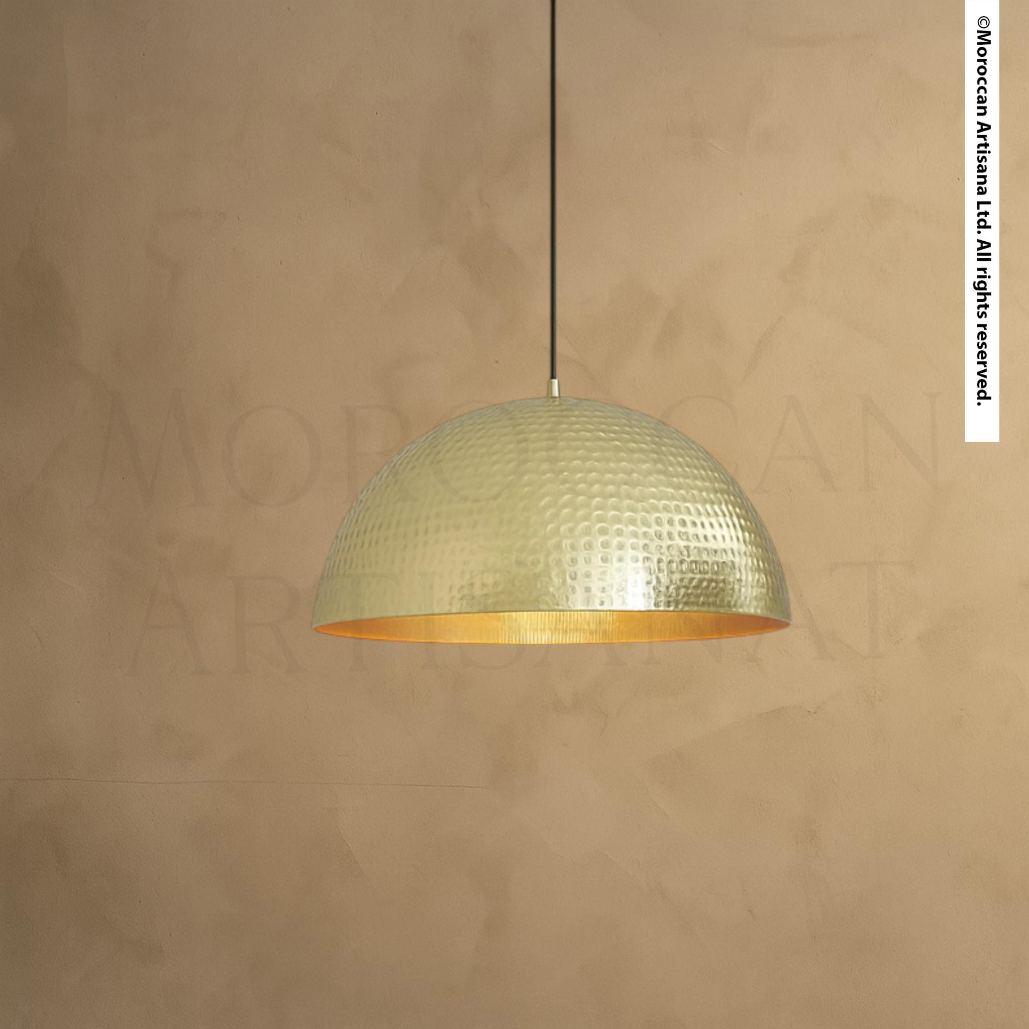 A modern, round pendant light with a textured, metallic finish hangs from the ceiling against a textured beige wall.