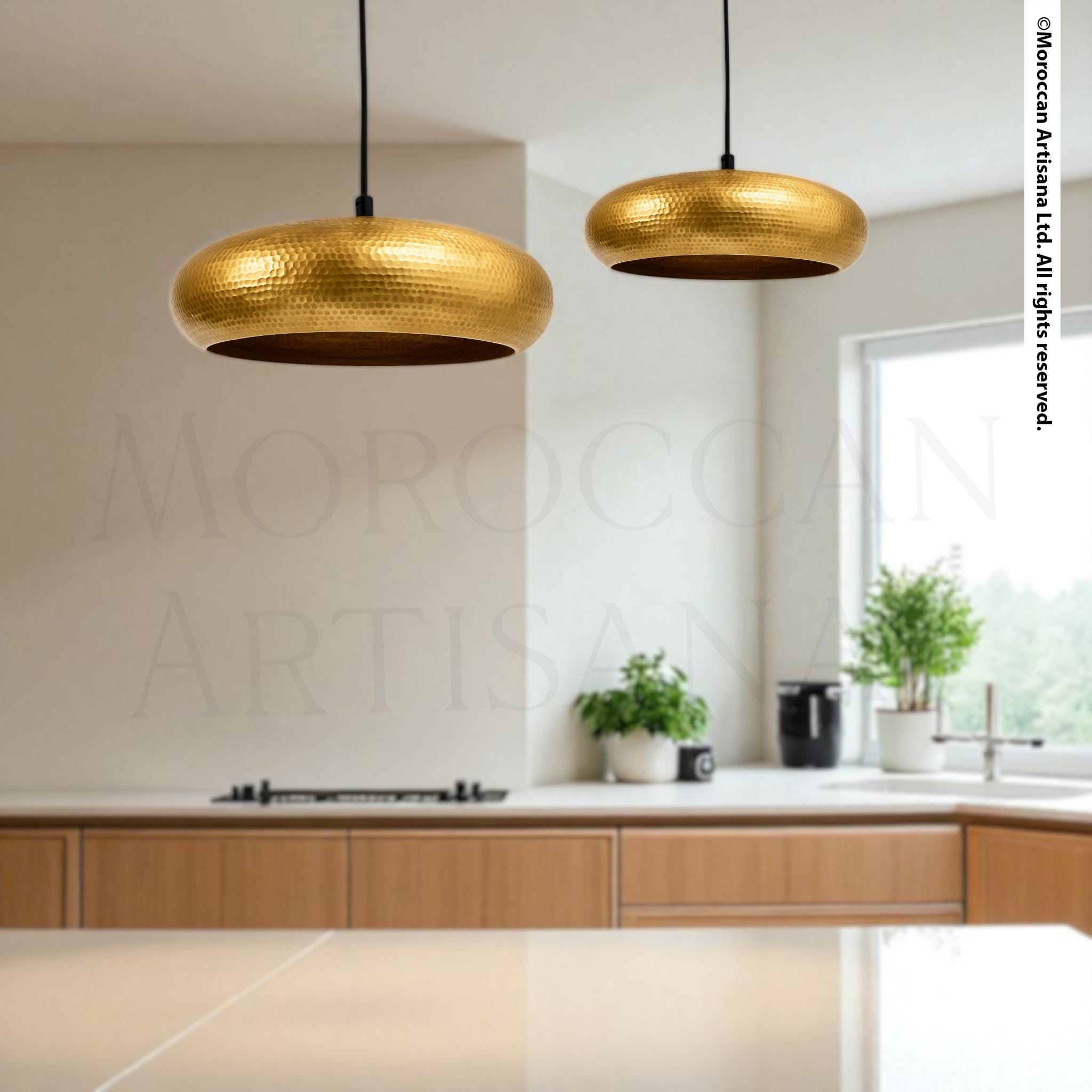 a modern kitchen with a large pendant light hanging above a wooden countertop. The kitchen has a minimalist design with white walls and wooden cabinets. There are two potted plants on the countertop, adding a touch of greenery to the space.