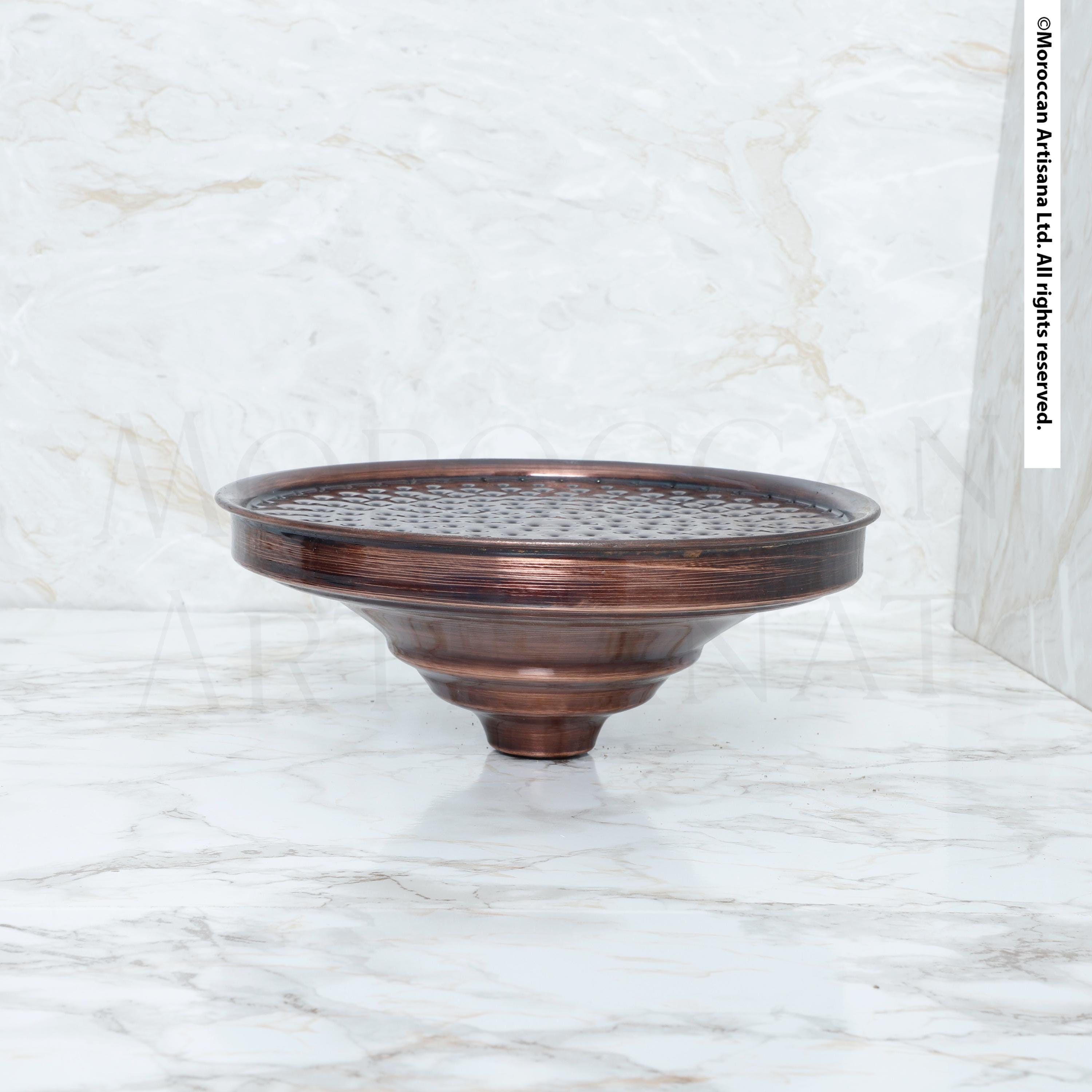 A bronze-colored metal object, possibly a bowl or vase, sits on a white marble surface.