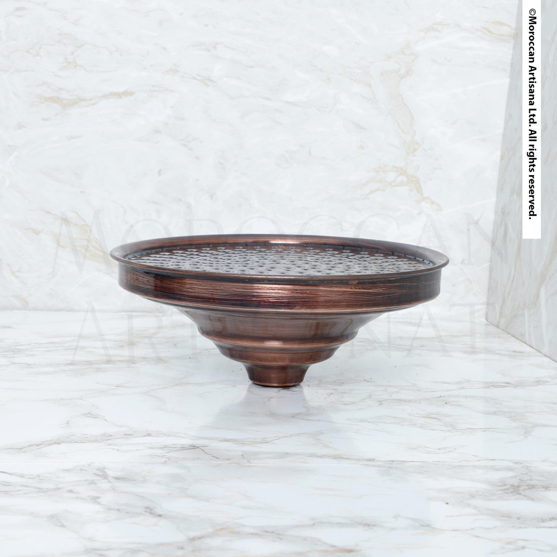 A bronze-colored metal object, possibly a bowl or vase, sits on a white marble surface.