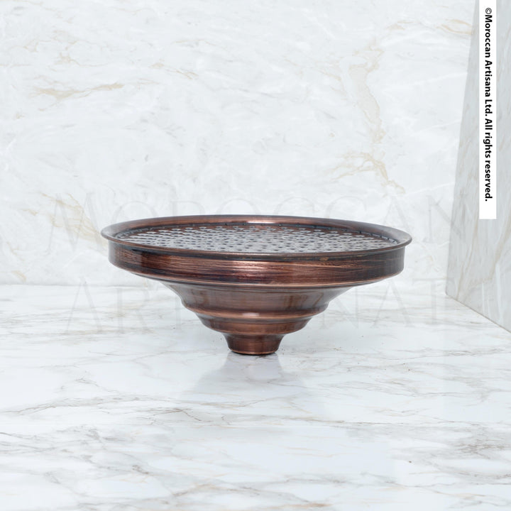 A bronze-colored metal object, possibly a bowl or vase, sits on a white marble surface.