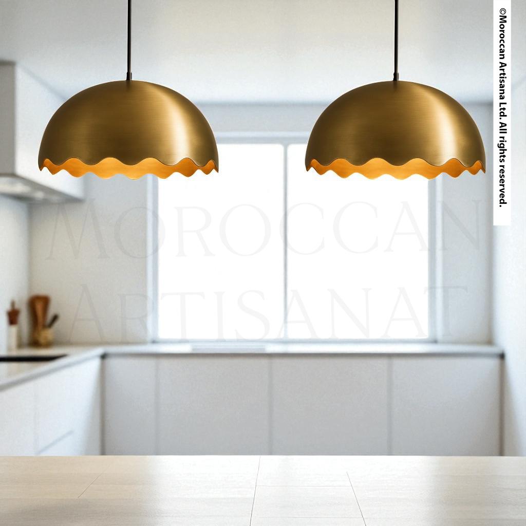two gold-colored pendant lights hanging from the ceiling in a kitchen setting.