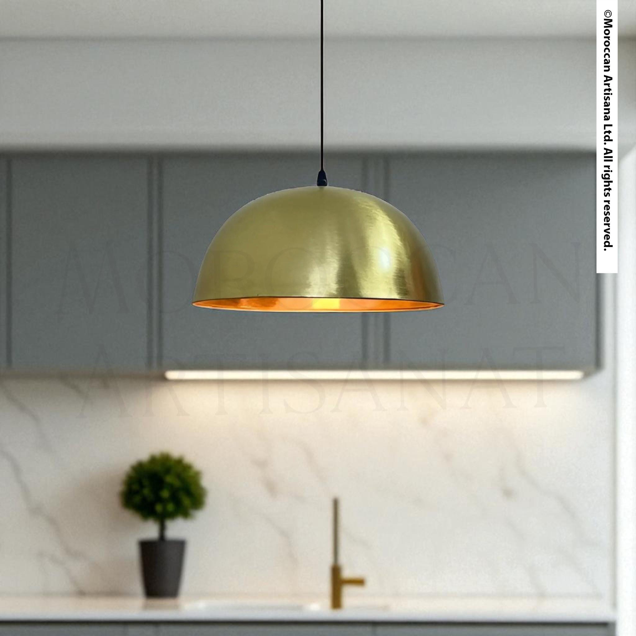 A modern kitchen with a gold-colored pendant light hanging above a sink, and a small potted plant on the countertop.