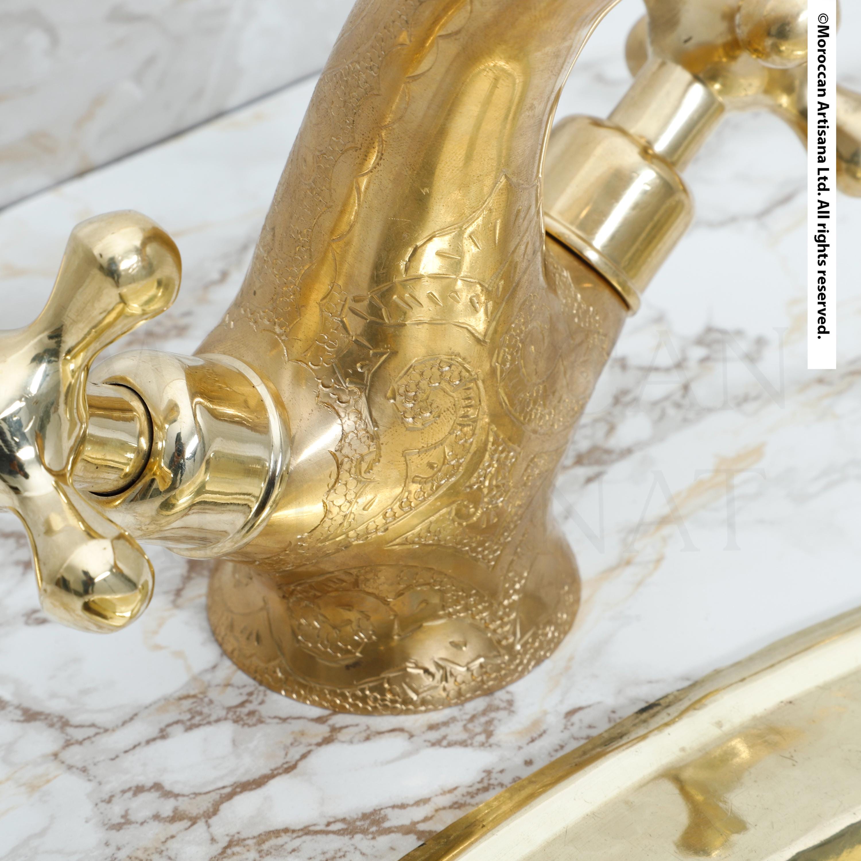 A close-up view of a decorative gold faucet with intricate patterns on its surface, set against a marble countertop.