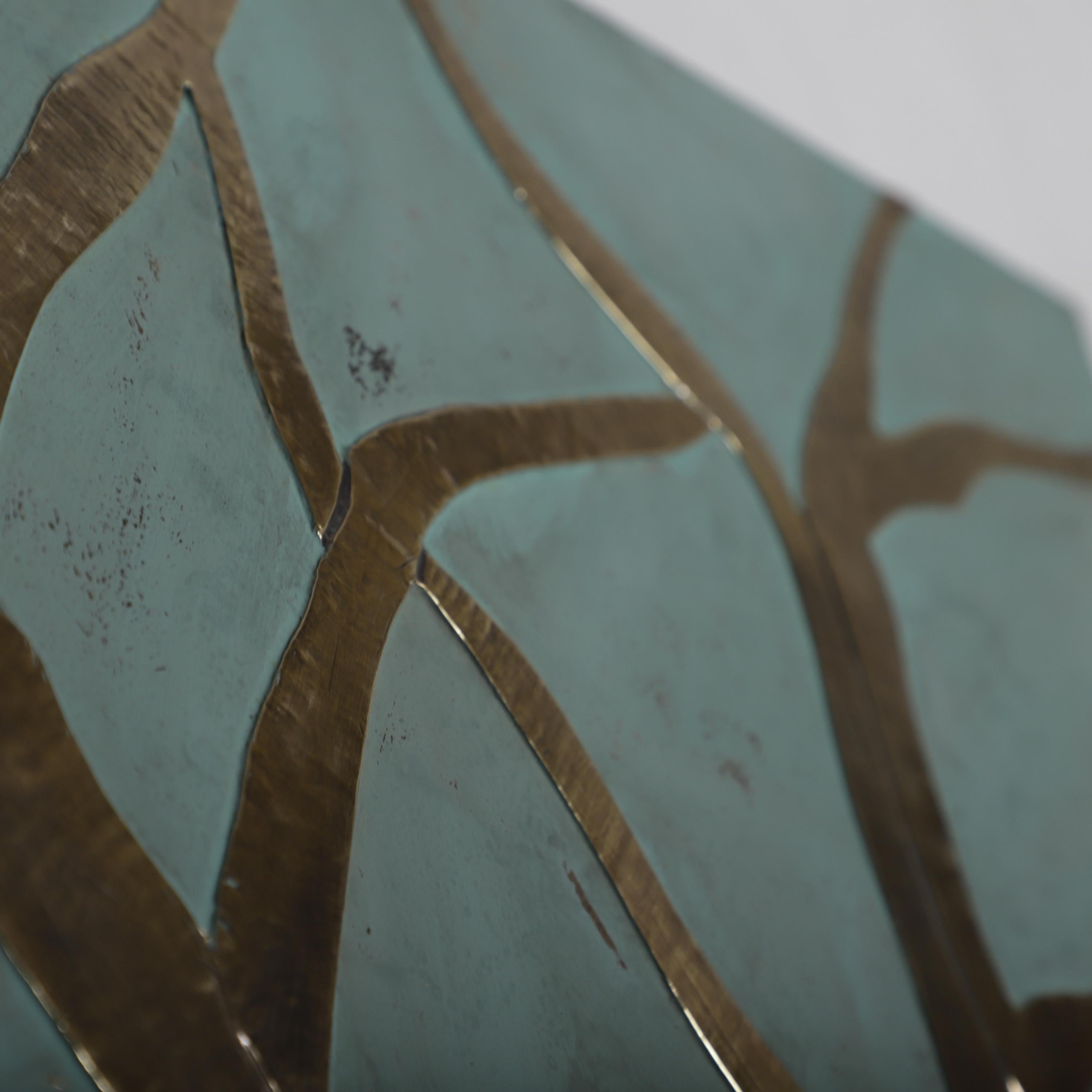 The image is a close-up of a piece of art with a blue and green color scheme, featuring a pattern of intersecting lines and shapes.