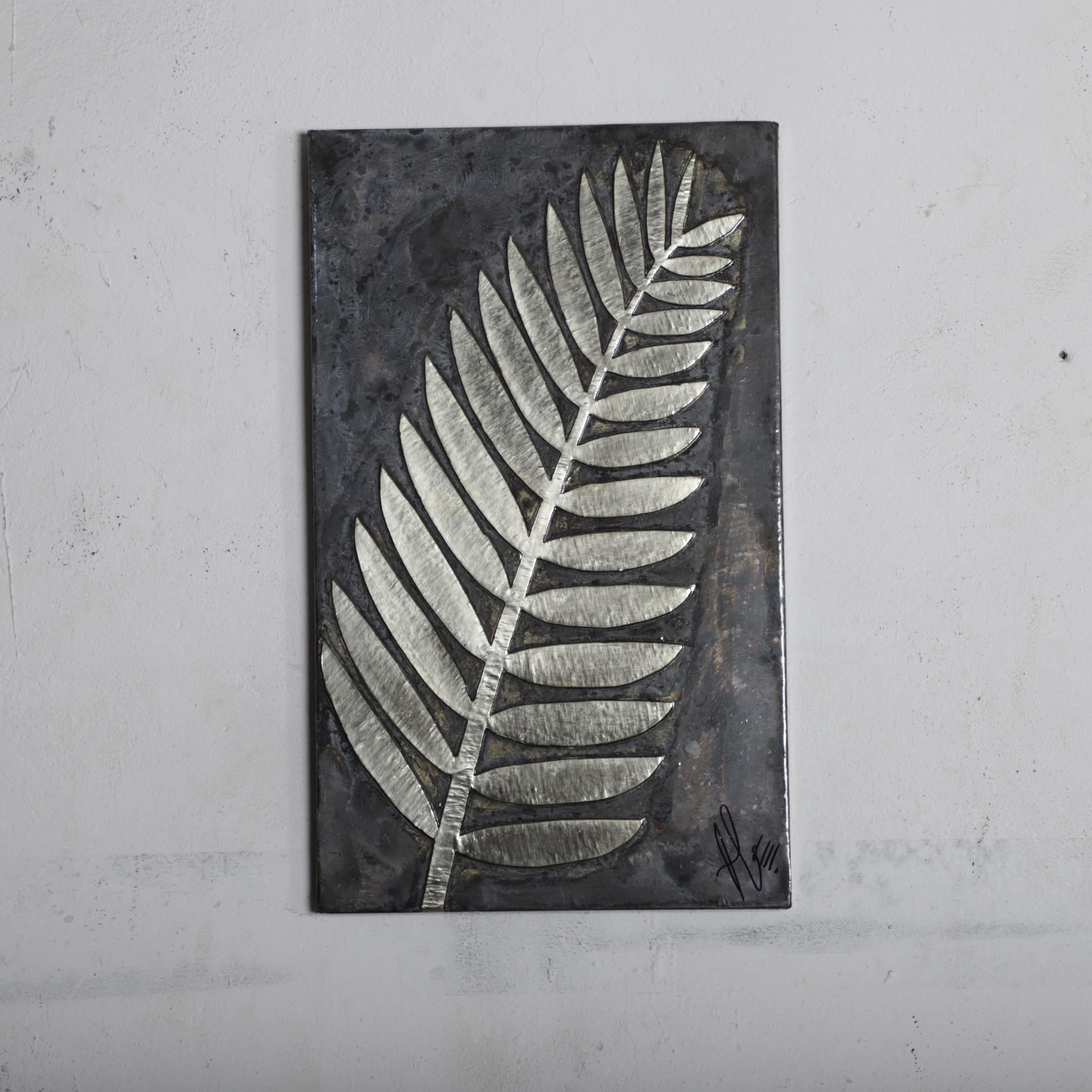 a close-up view of a metal leaf with a textured surface, mounted on a wall.