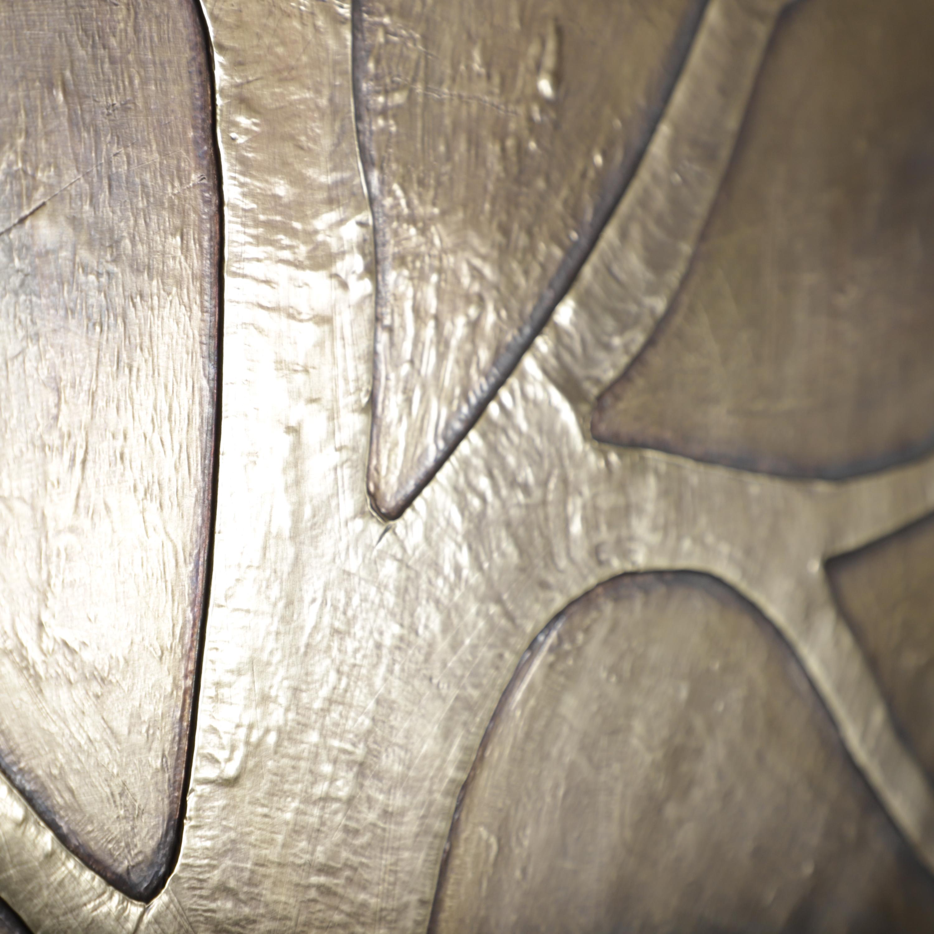 The image is a close-up of a metallic surface with a textured, shiny appearance. The surface appears to be made of a shiny, metallic material, possibly brass or bronze. The image does not contain any discernible text or countable objects, and the focus is on the texture and surface quality of the material.