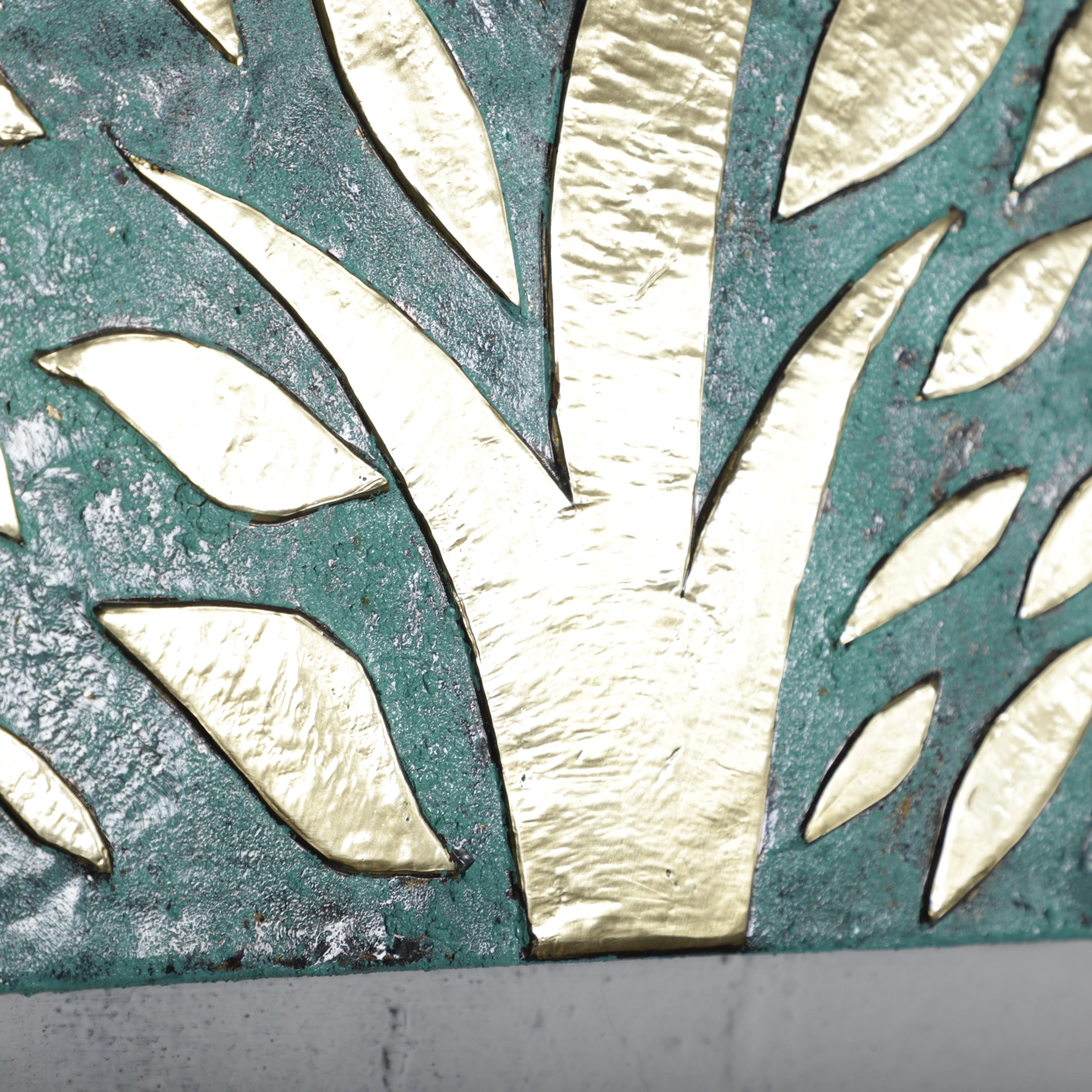 a close-up view of a decorative piece with a textured surface, possibly made of metal or ceramic. The piece appears to be a wall hanging or a similar type of artwork, with a pattern of leaves or branches in shades of green and gold. The image does not contain any text or other discernible objects or actions.