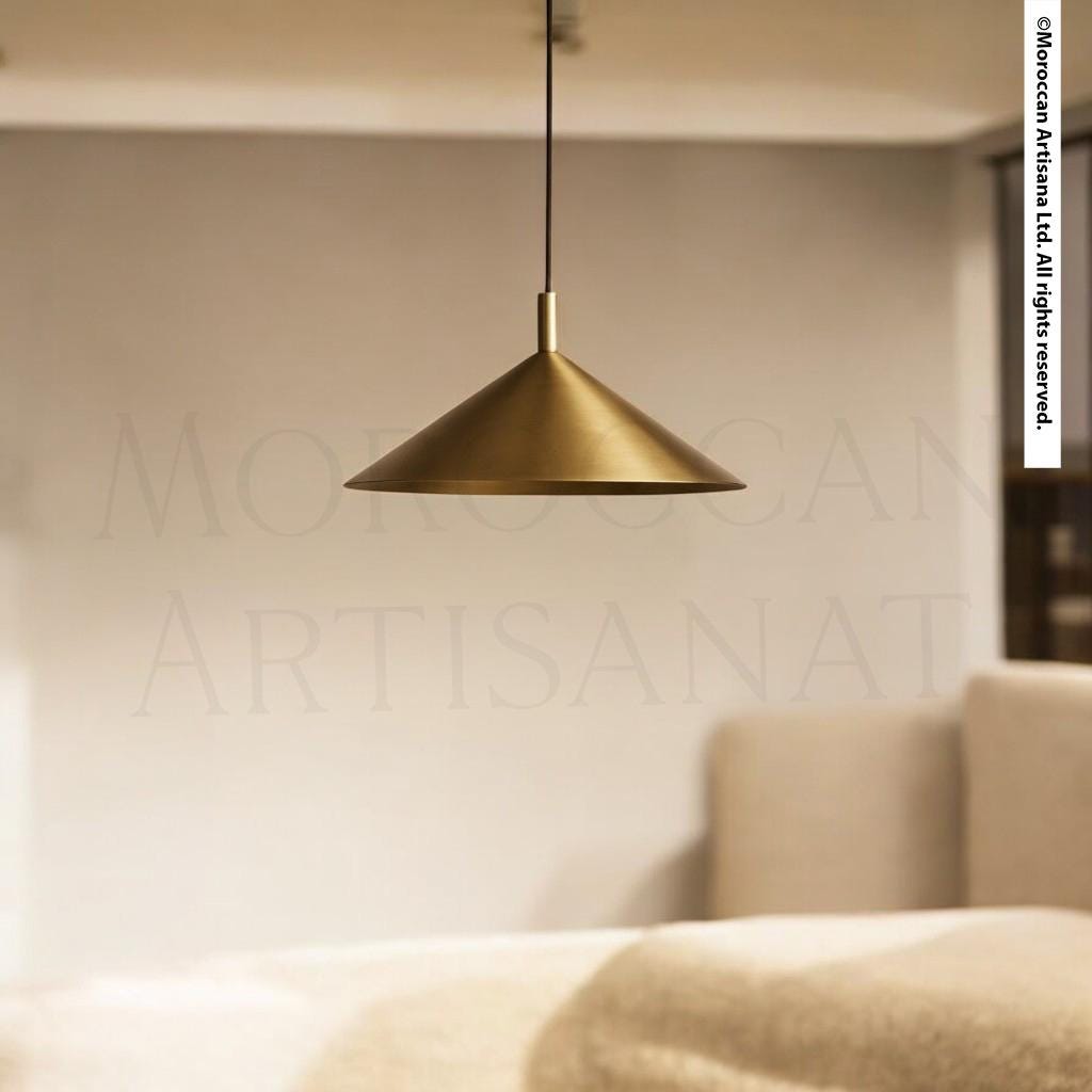 A gold-colored pendant lamp hangs from the ceiling in a room with a beige sofa and a white wall in the background.