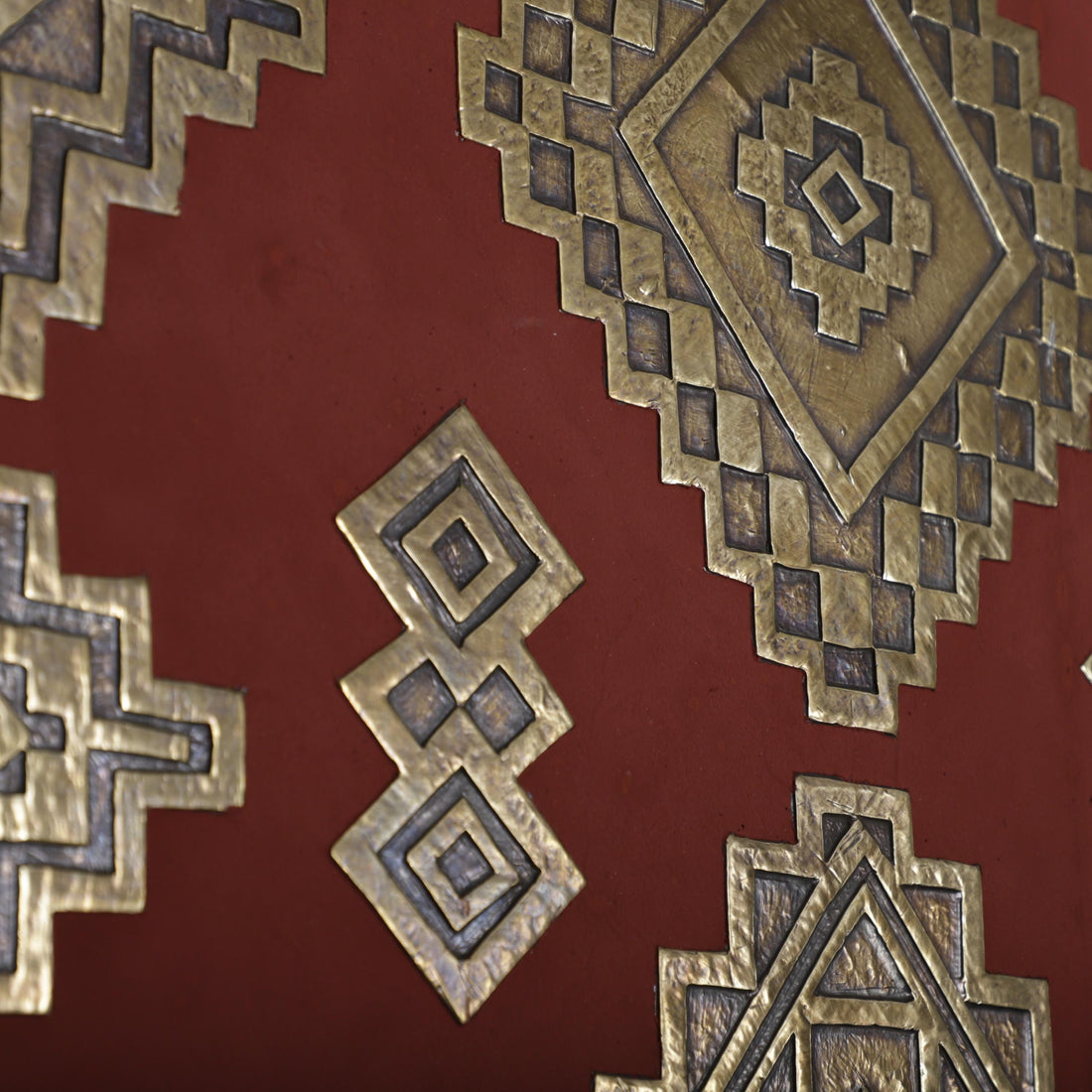 a close-up view of a red surface adorned with intricate geometric patterns and designs, including a diamond-shaped pattern and a diamond-shaped design with a smaller diamond-shaped pattern within it.