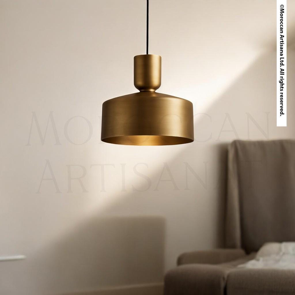 A gold-colored pendant light hangs from the ceiling in a room with a beige sofa and a white wall in the background.