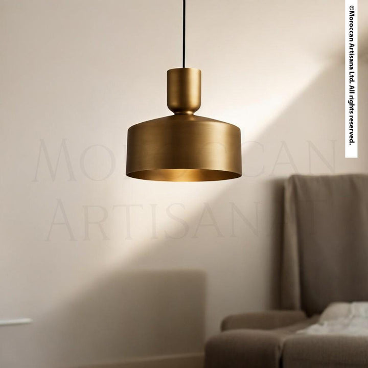 A gold-colored pendant light hangs from the ceiling in a room with a beige sofa and a white wall in the background.