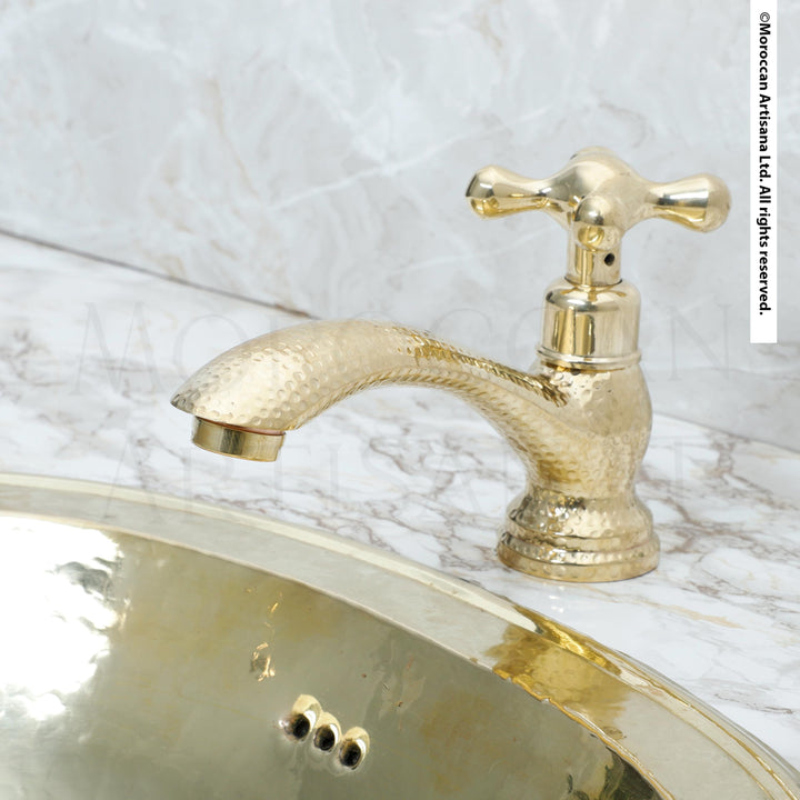 A gold-colored faucet with a textured finish is positioned above a marble sink.