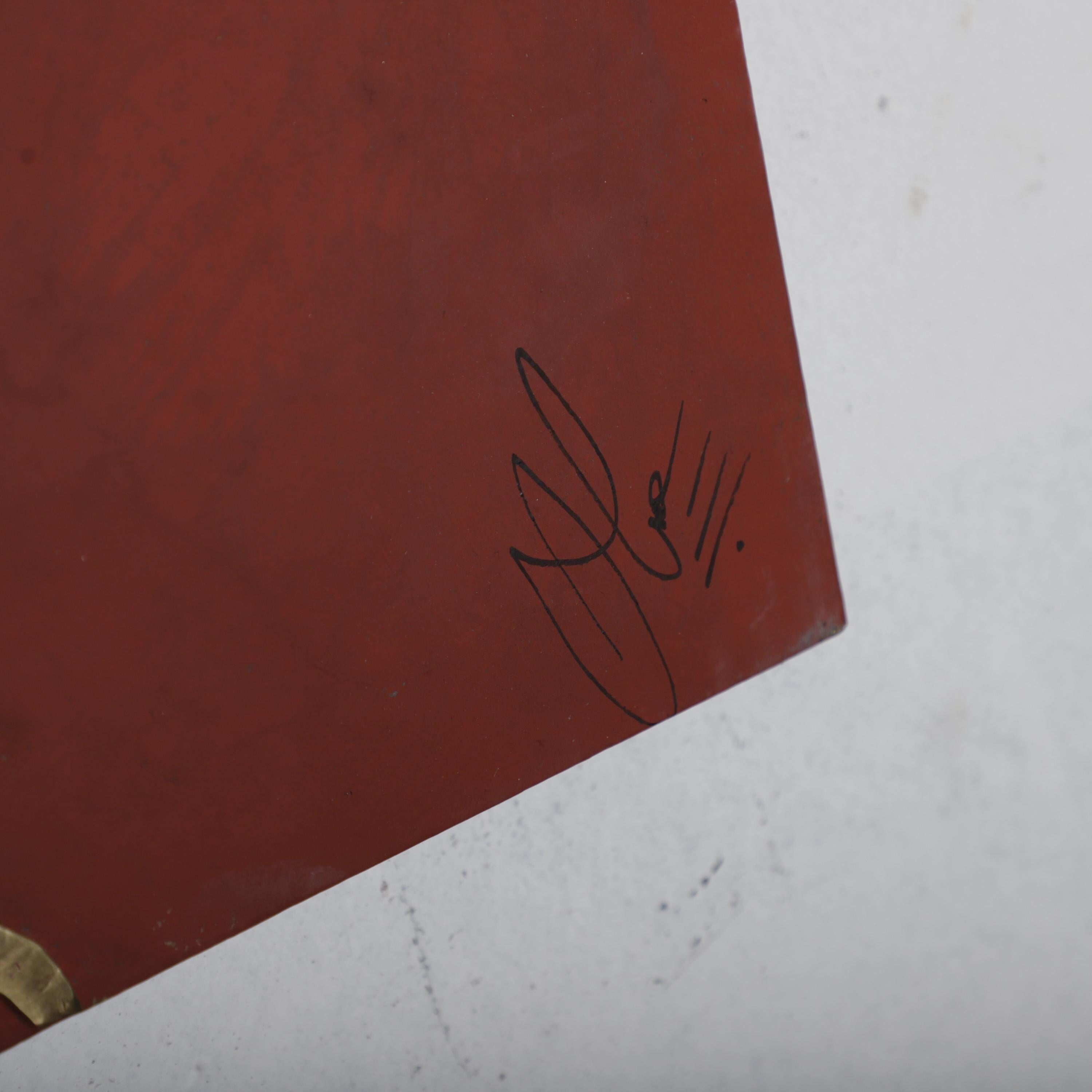 a close-up view of a red surface with a black signature or mark in the corner.