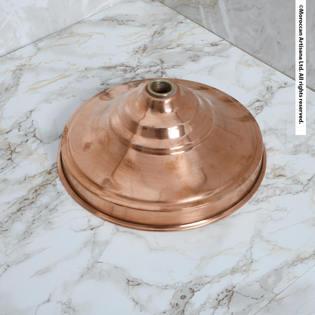 a copper-colored metal object, possibly a lampshade or a light fixture, sitting on a marble surface.