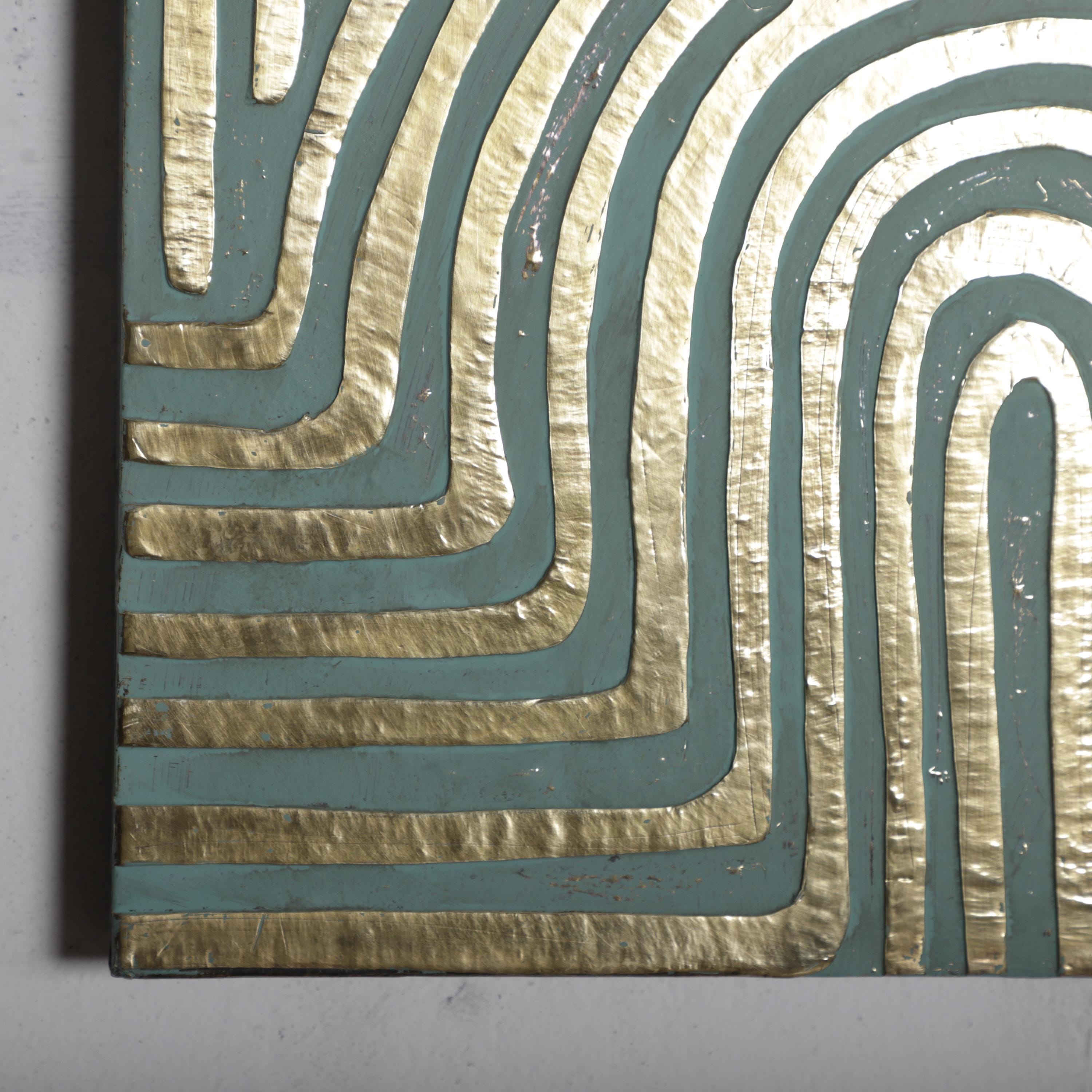 a close-up view of a piece of art with a striking geometric pattern. The pattern consists of curved lines in shades of blue and gold, creating a visually captivating design. The artwork is displayed on a white surface, which highlights the colors and shapes within the piece.