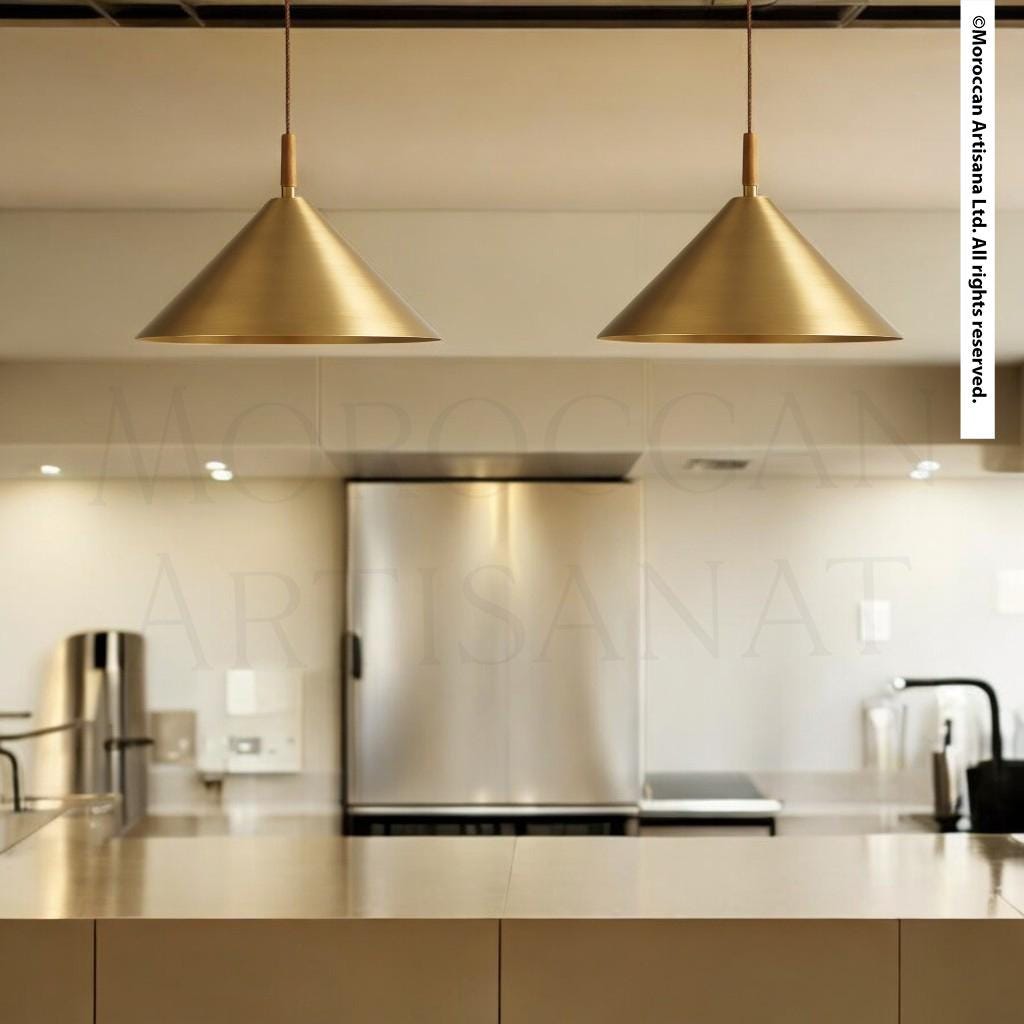 a modern kitchen with a sleek, minimalist design. The focal point is a pair of golden pendant lights hanging above a countertop, which is made of a shiny, reflective material. The kitchen also includes a stainless steel refrigerator and a sink, contributing to the overall contemporary aesthetic.