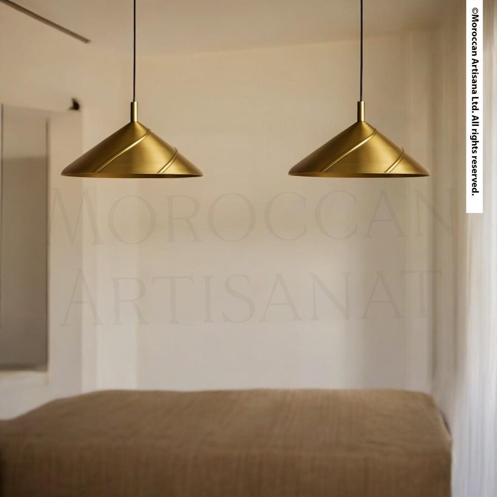 two gold pendant lights hanging from the ceiling, illuminating a room with a bed in the background.