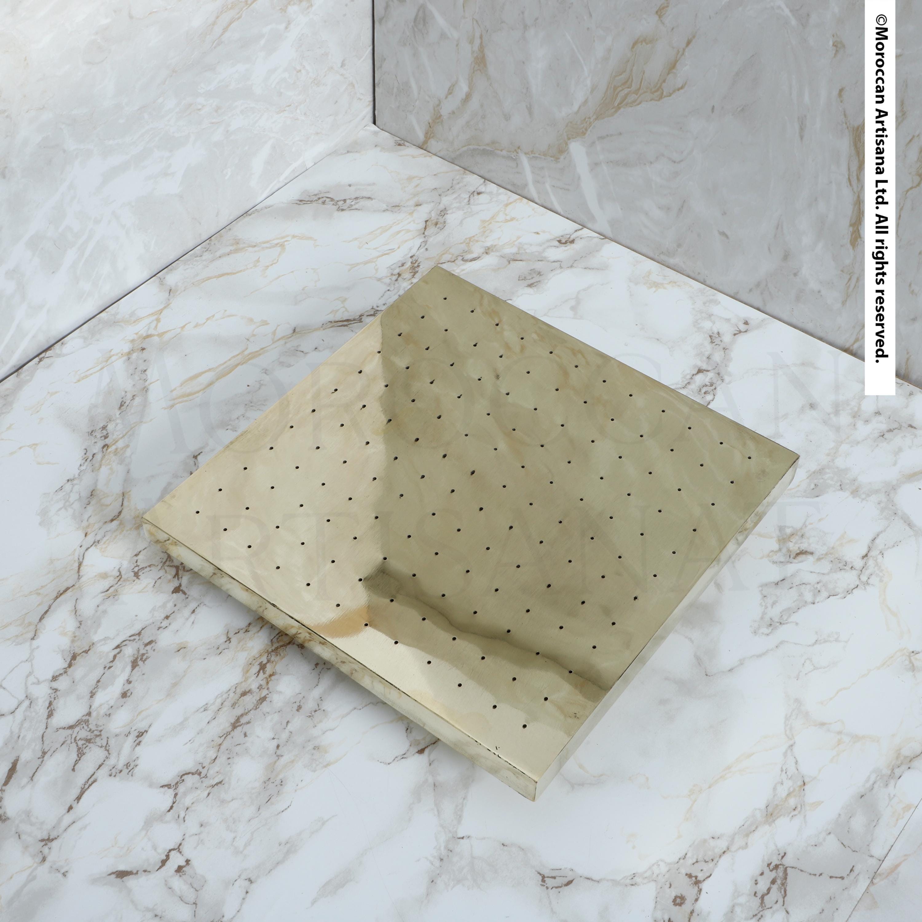 a square, metallic surface with a grid-like pattern of small holes or dots on it, placed on a marble countertop or floor.