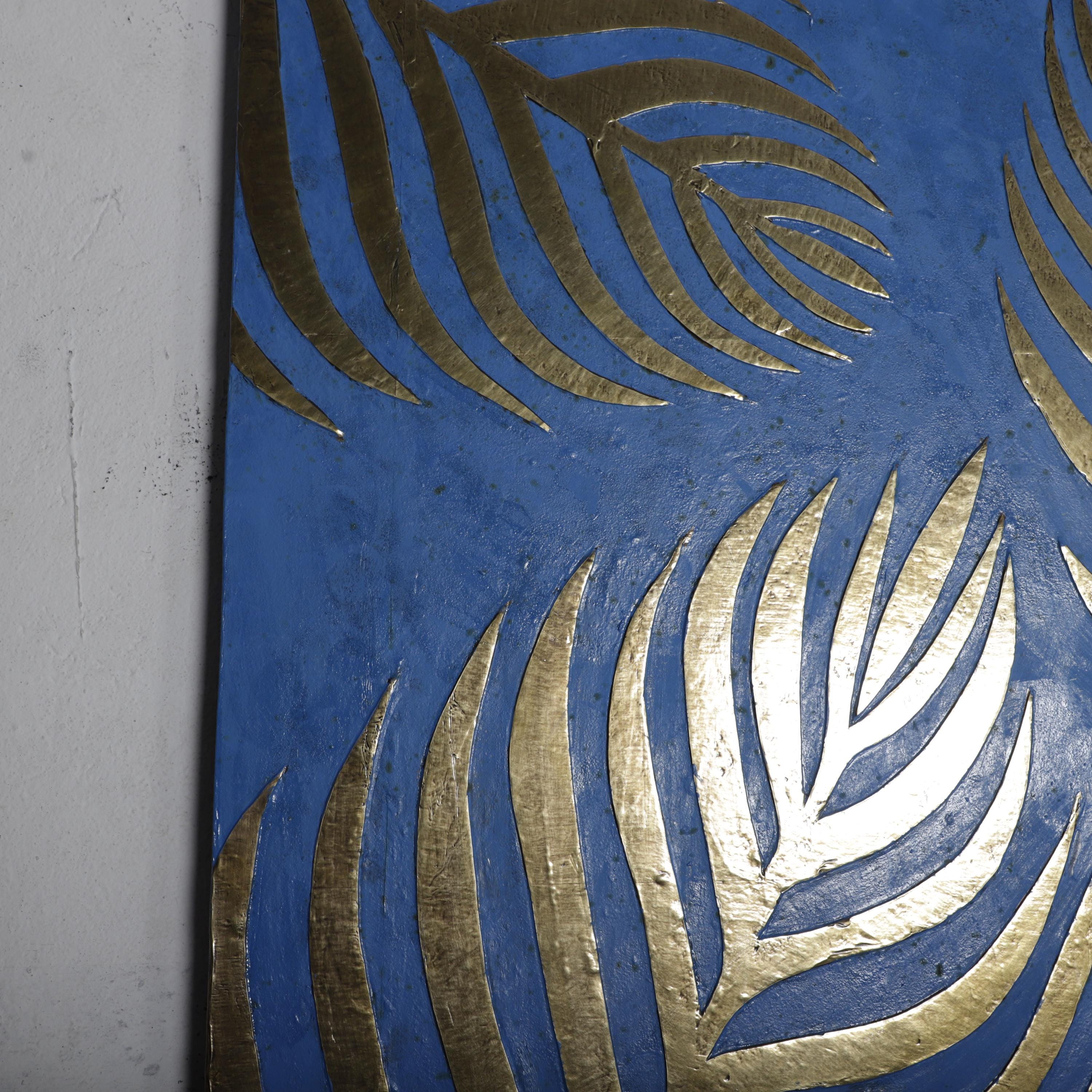 a close-up view of a blue surface with a gold leaf pattern. The pattern consists of overlapping palm leaves with a metallic sheen, creating a visually striking contrast against the blue background.