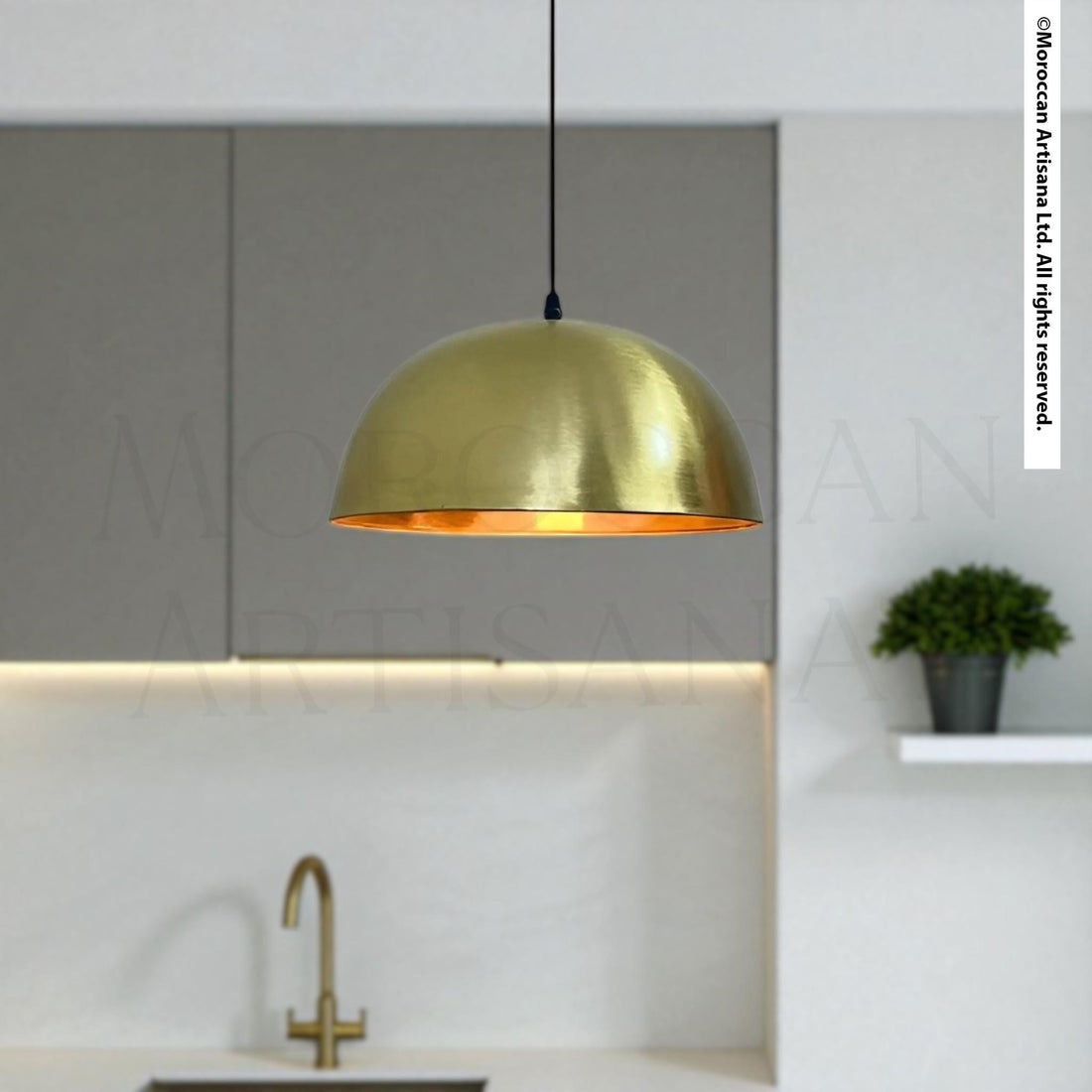 a modern kitchen with a gold pendant light hanging above a sink, a plant on a shelf, and a gray cabinet in the background.