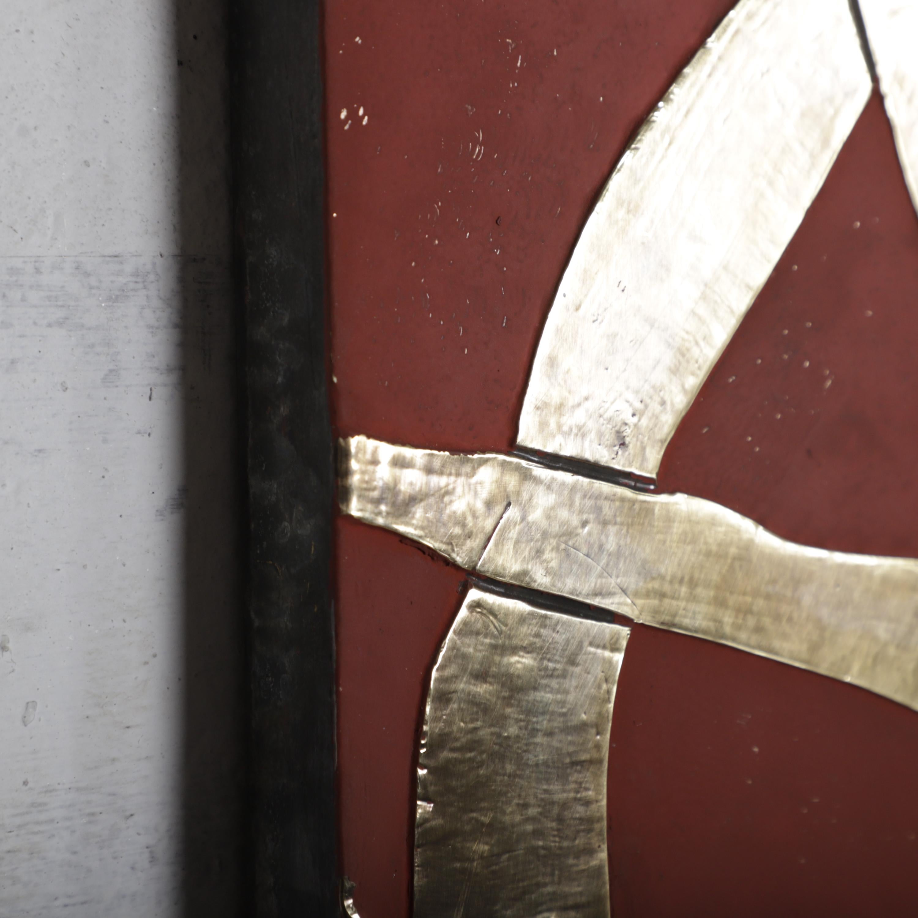 a close-up view of a red surface with a metallic, curved object resembling a bird or a symbol. The object appears to be made of a shiny material, possibly metal, and is positioned on the right side of the image.